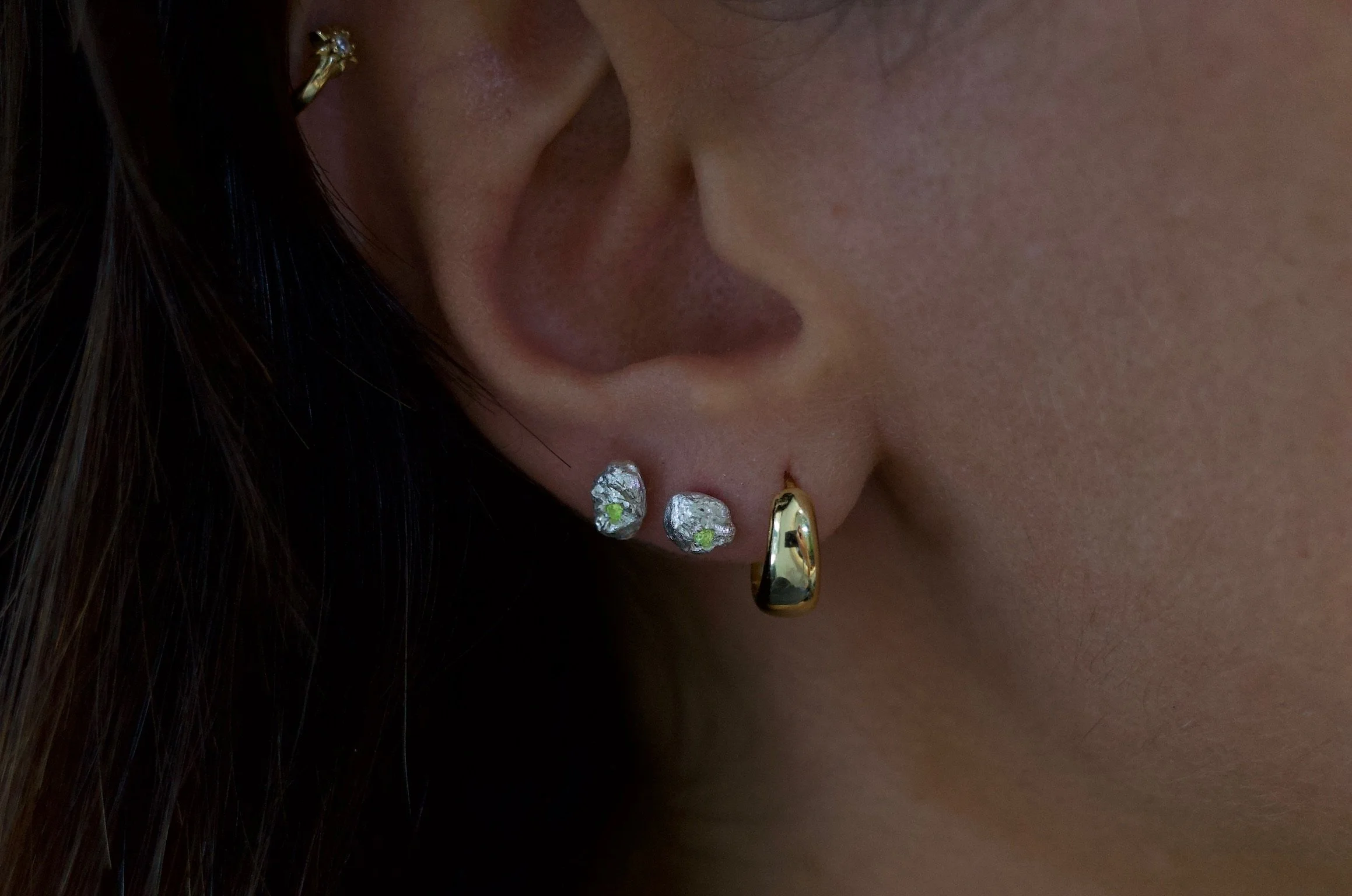 Textured sterling silver studs with a neon green stones. The studs are mismatched and in an ear