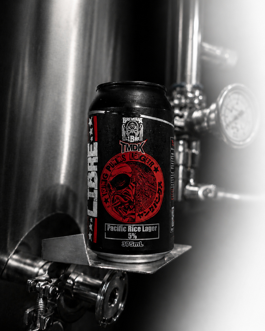 A black can of Pacific Rice Lager beer with red and white labeling placed on metallic brewing equipment.