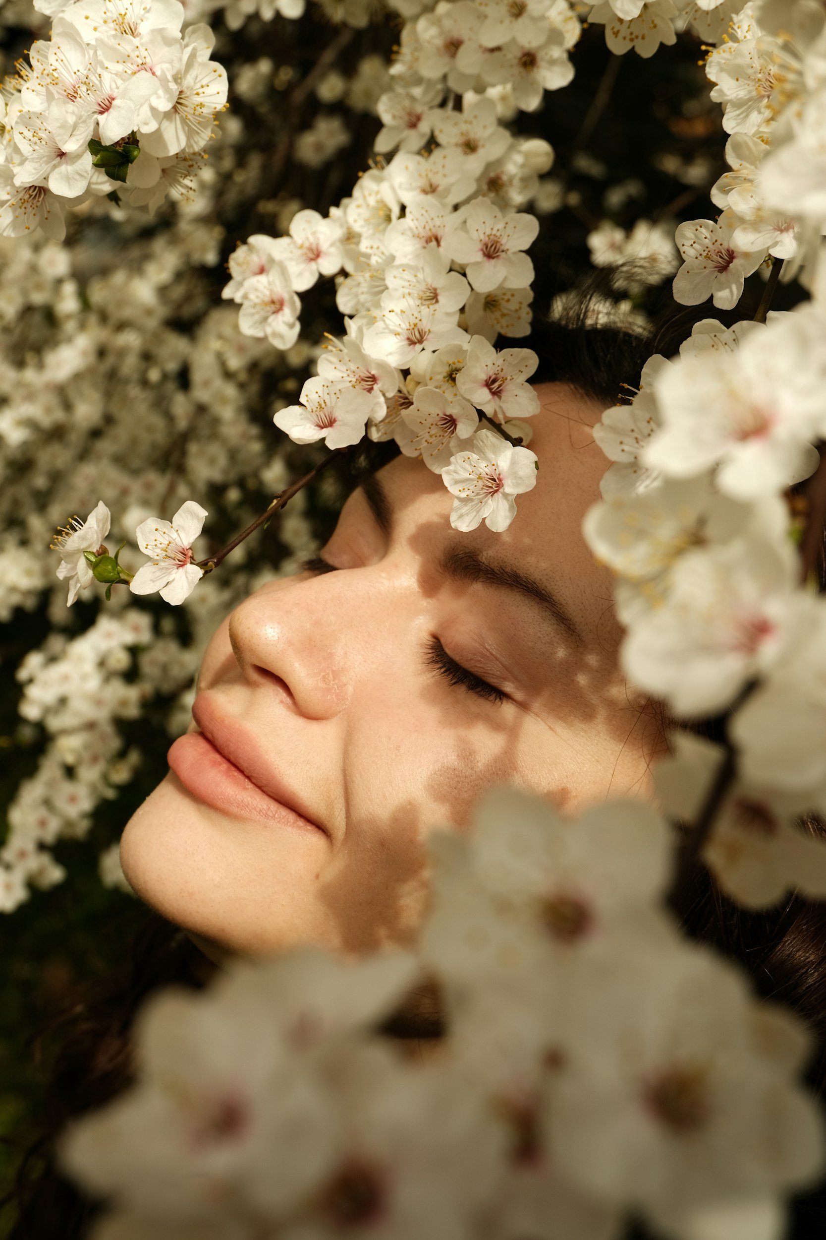 Woman with closed eyes surrounded by white cherry blossoms