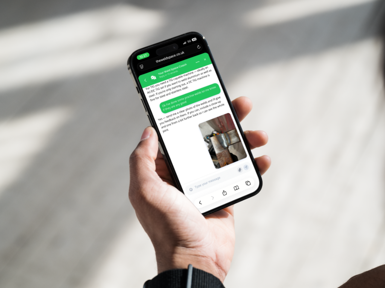 Hand holding a smartphone displaying a chat conversation on a webpage.