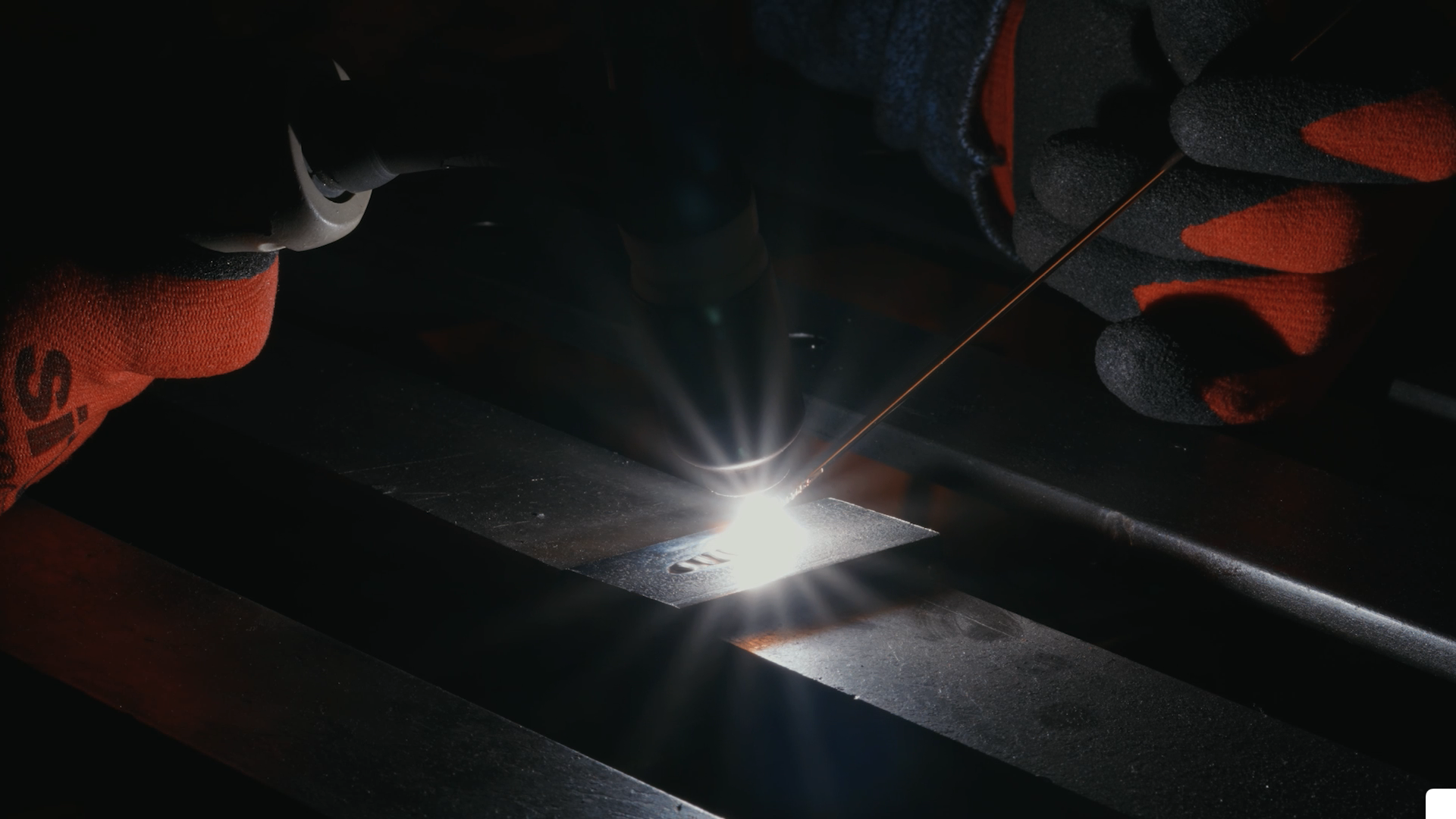 A person welding metal, wearing gloves, with a bright welding spark and metal pieces.