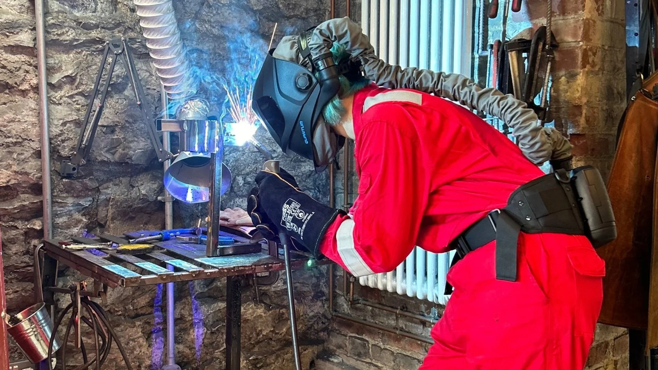 welder wearing overalls and welding helmet.
