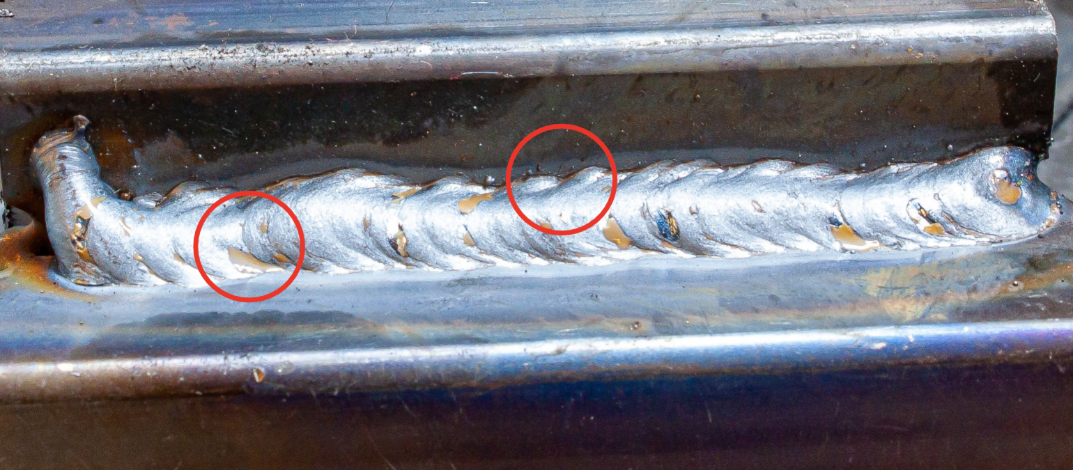 Close-up of a welded metal joint with visible heat marks and two circled areas indicating weld flaws or imperfections.