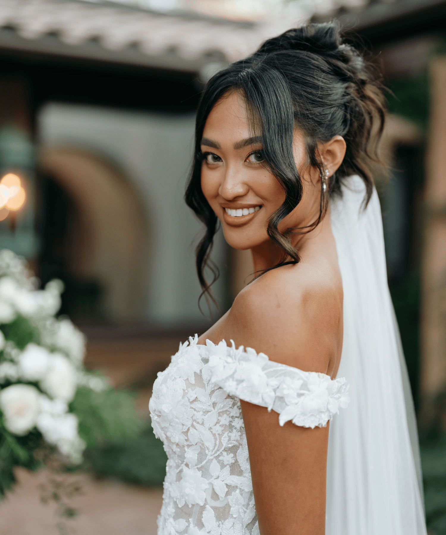 A woman in a white off-shoulder wedding dress smiling outdoors.