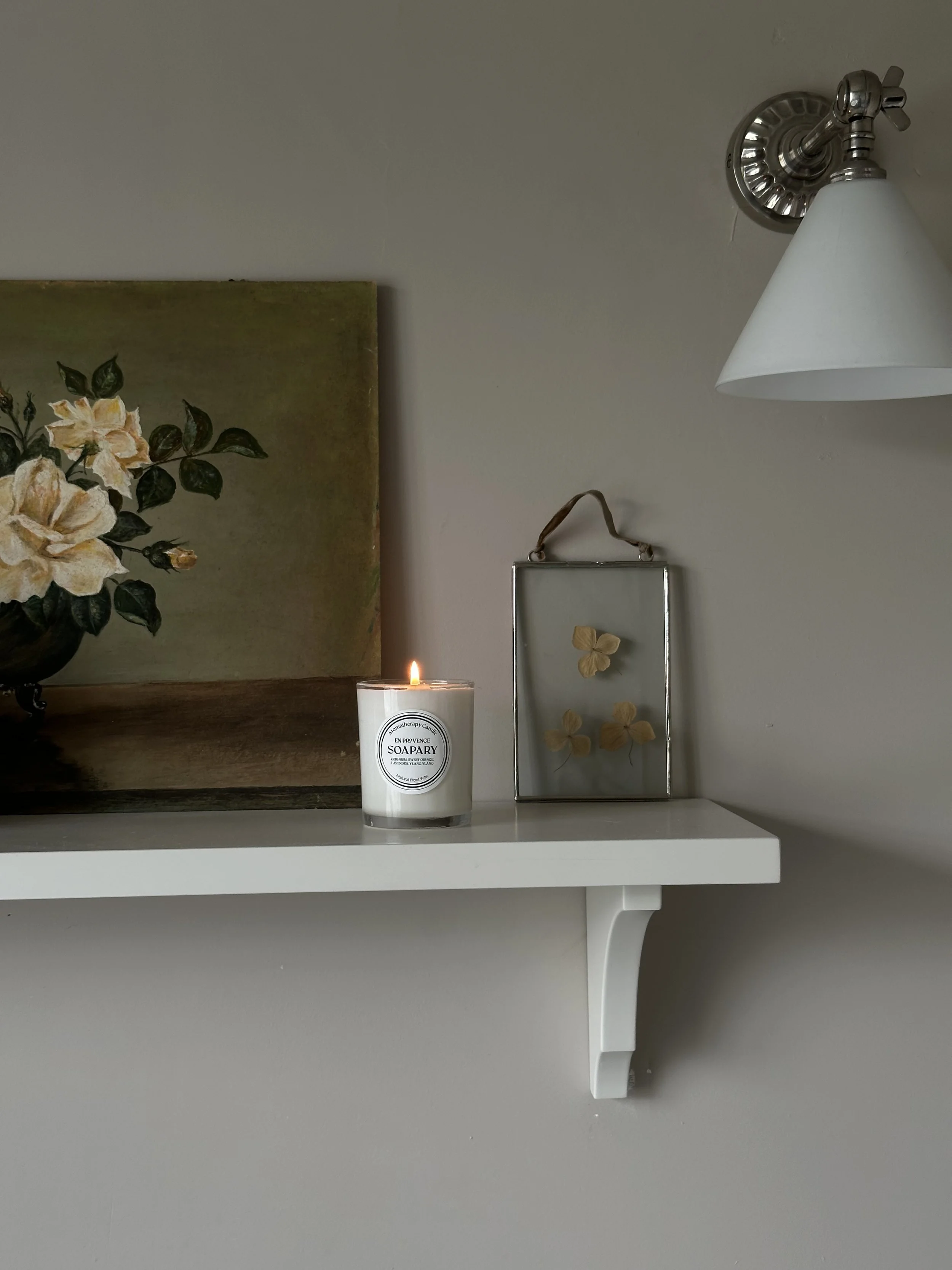 candle on shelf with vintage artwork behind