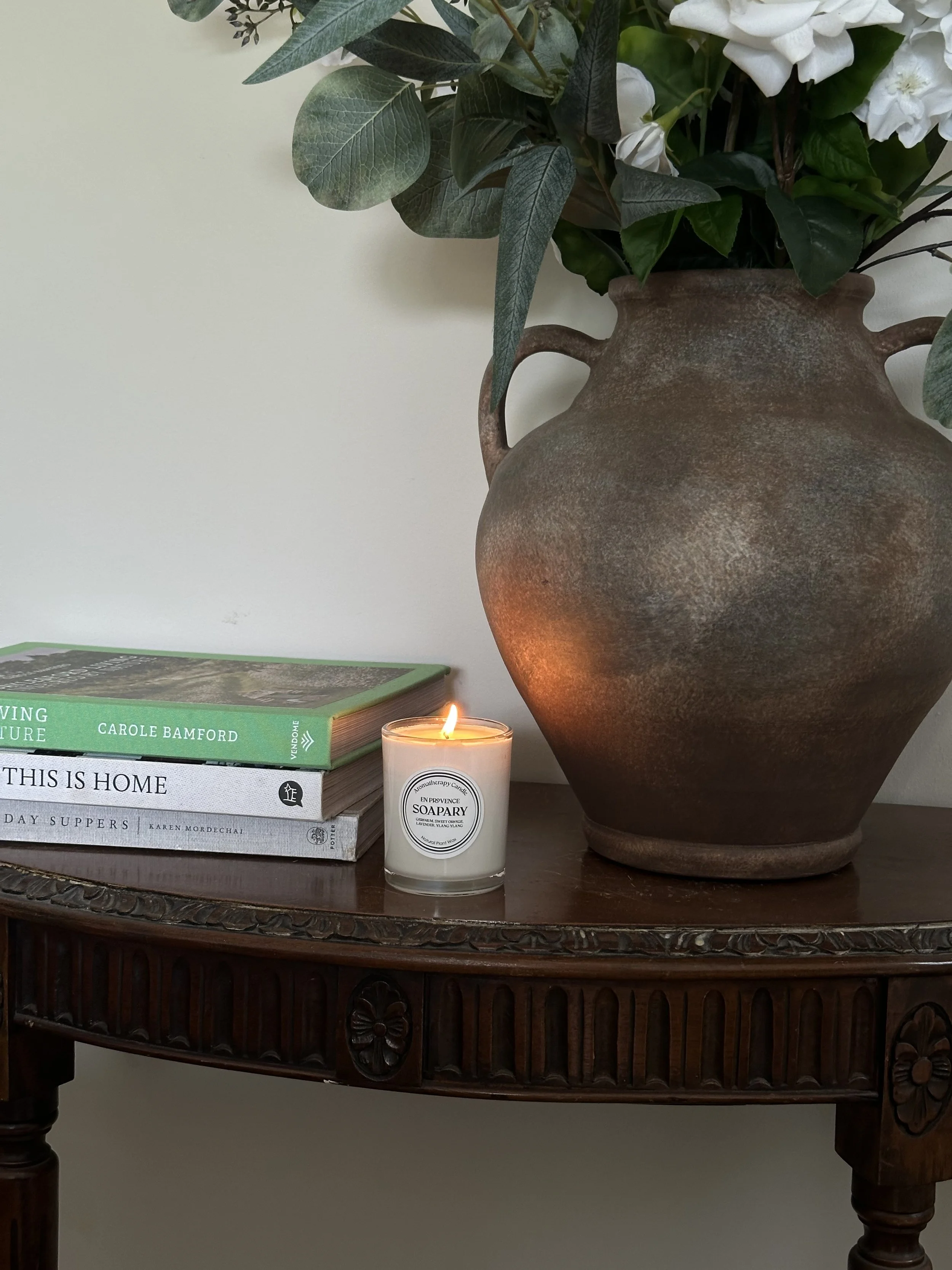 botanical candle lit next to a stack of interiors books and bronze vase
