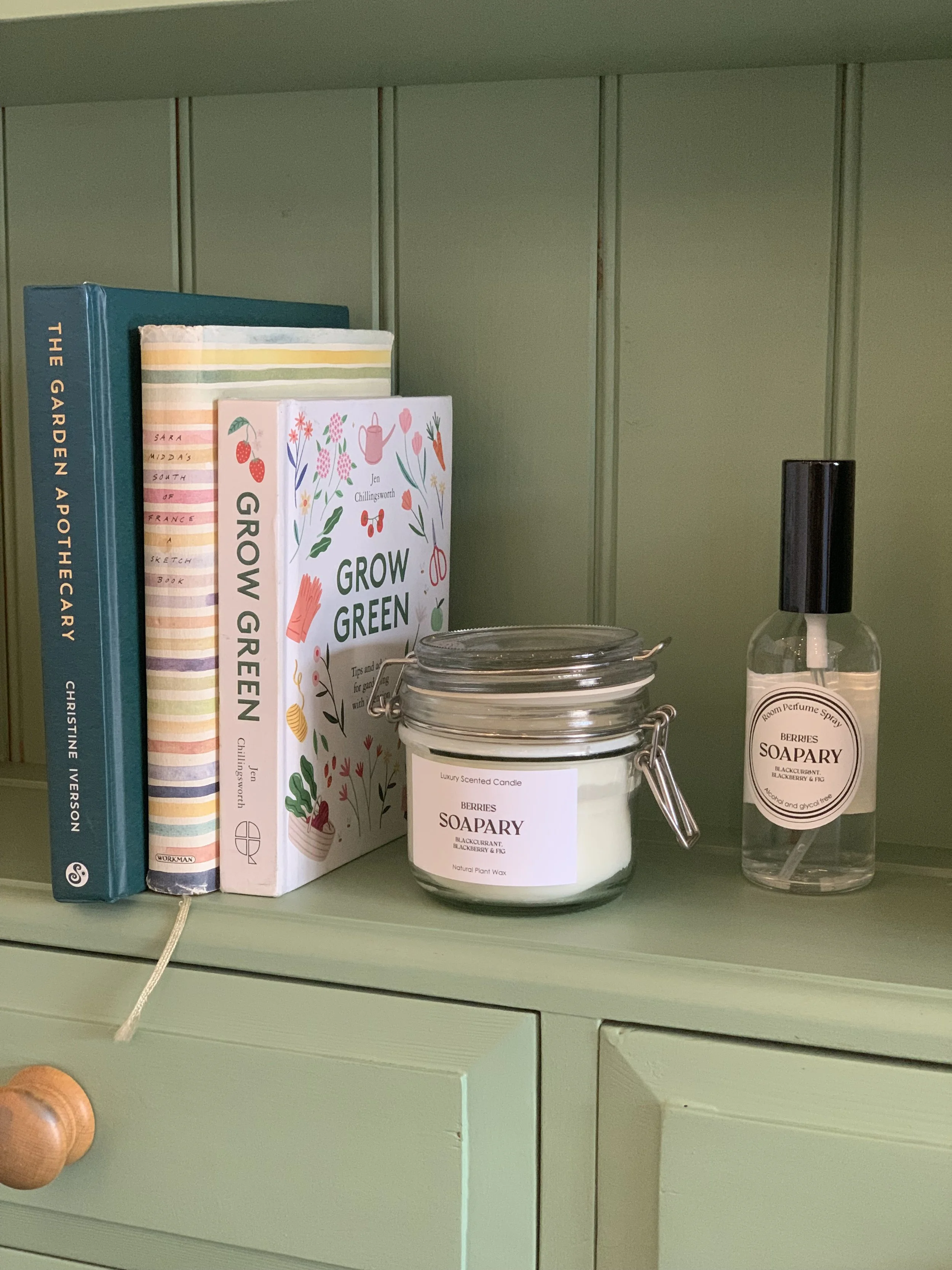 Books, a candle, and a spray bottle on a green shelf.