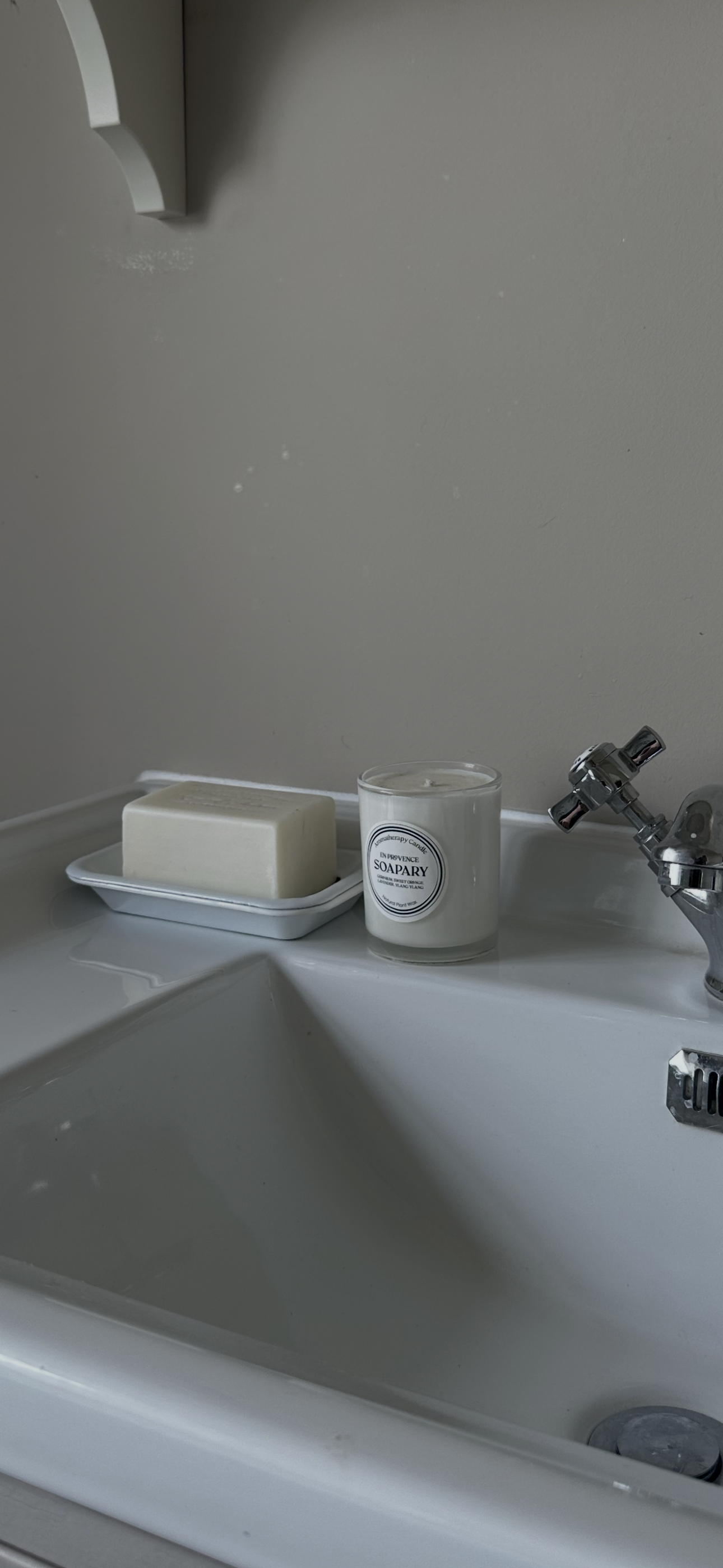 Bathroom sink with a soap dish holding soap and a candle labeled "Soapary" on a white tray, alongside a silver sink faucet.