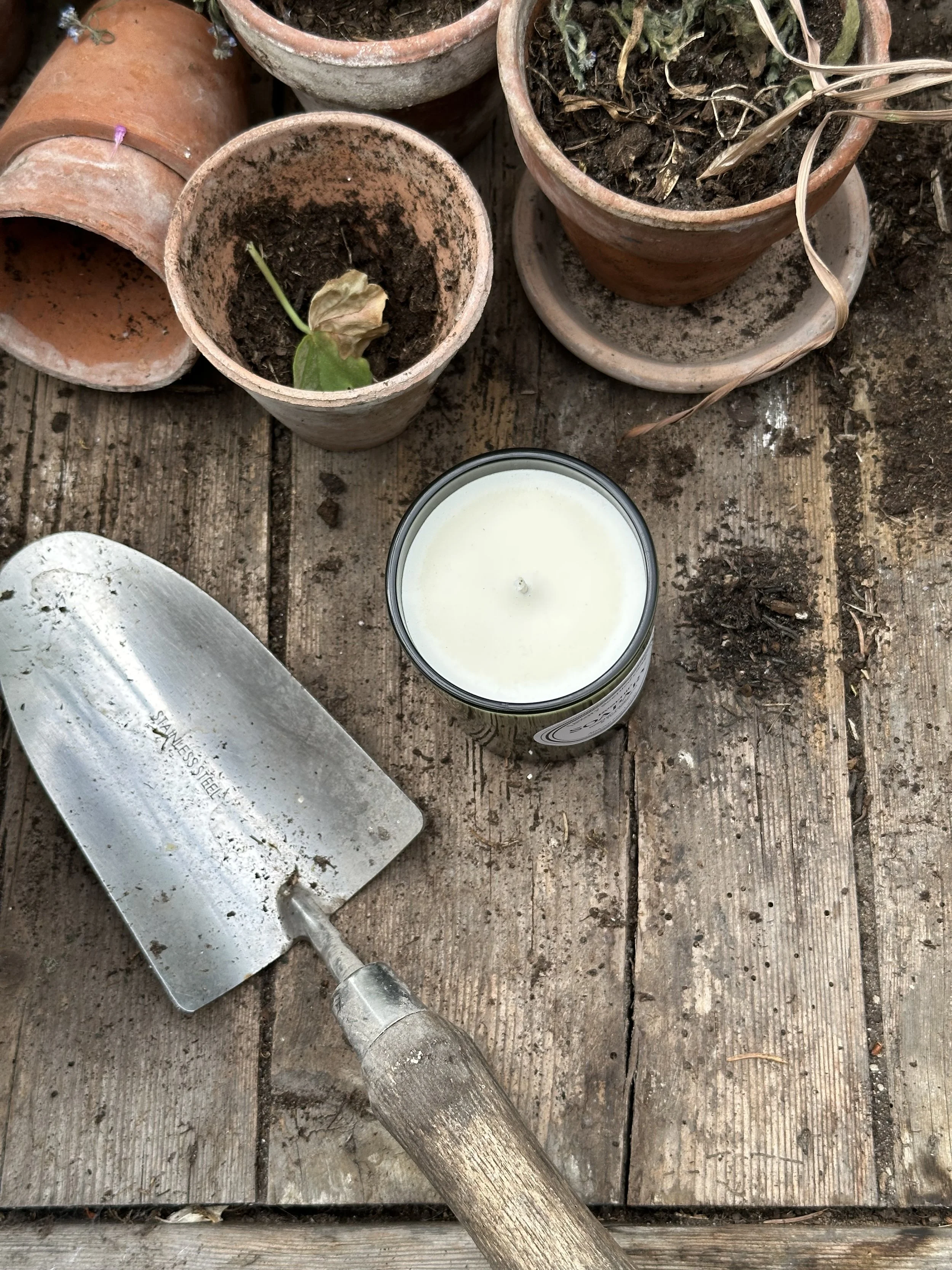 potting bench with terracotta pots, soil and a green glass candle