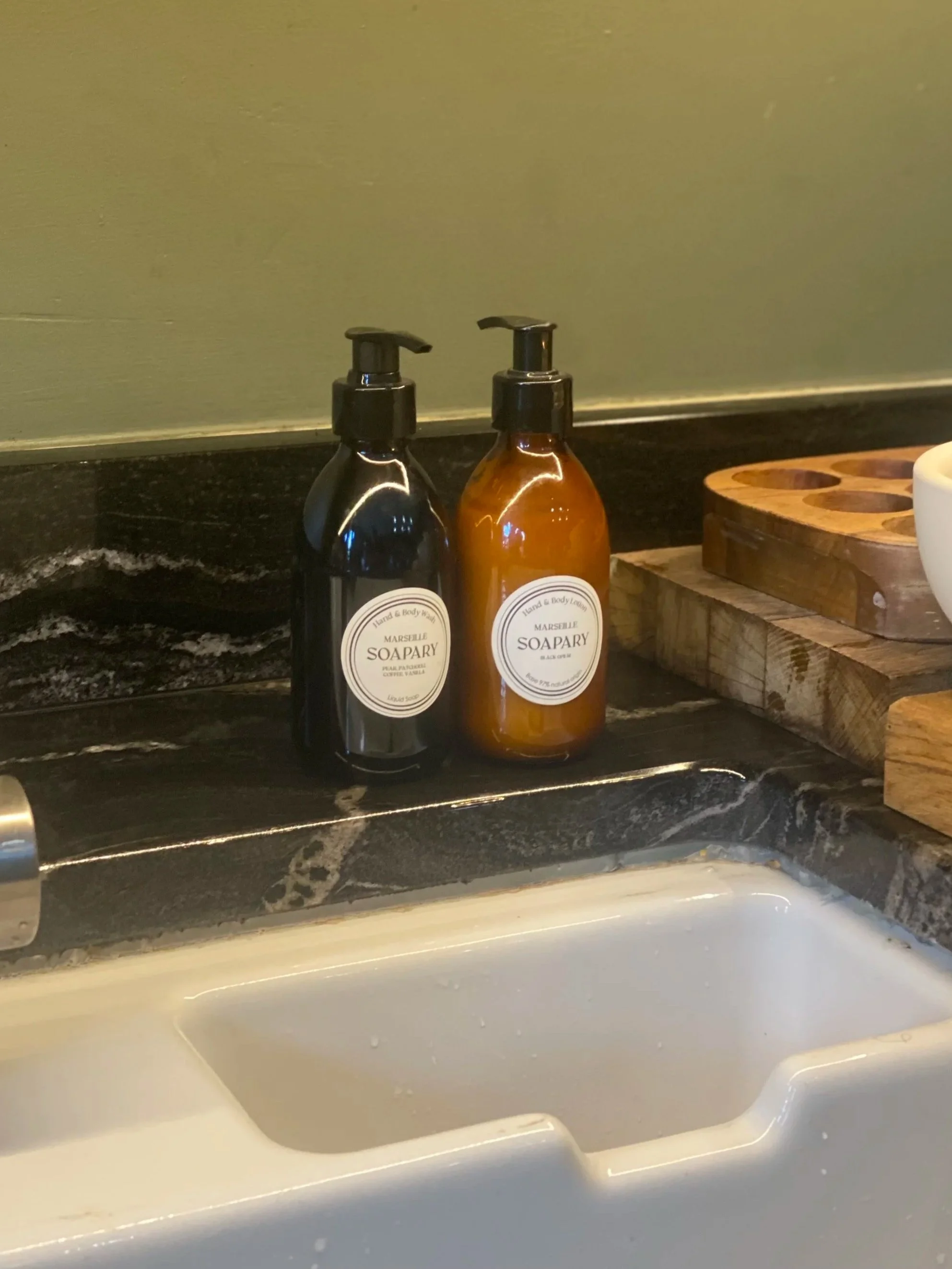 hand wash and lotion stood at a Belfast sink with green kitchen wall behind