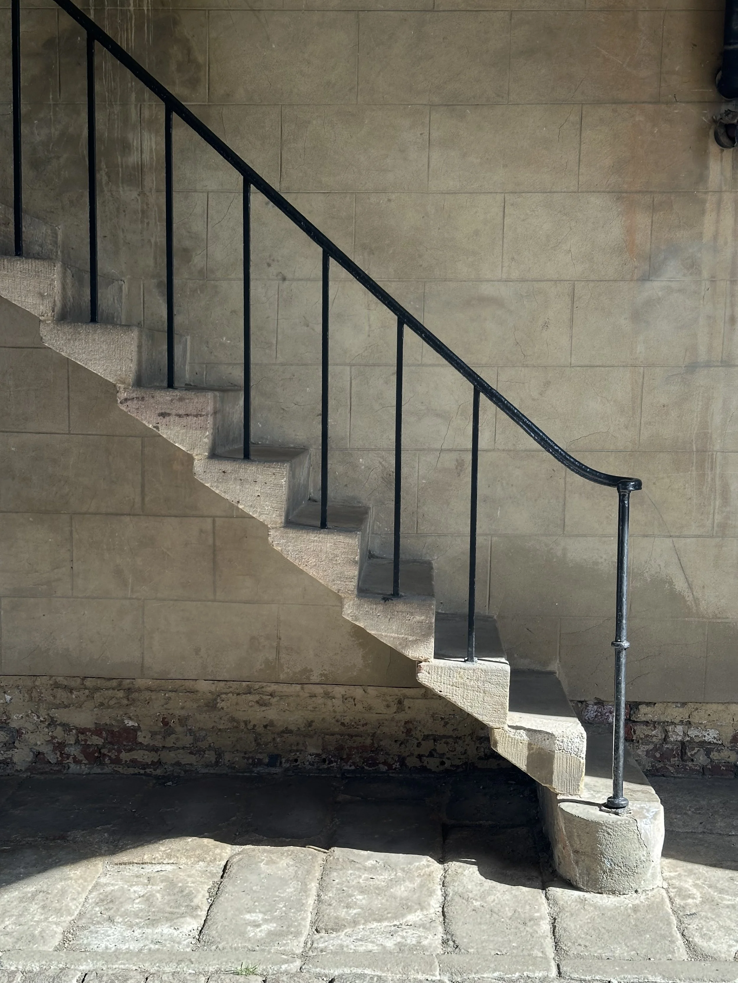 A concrete staircase with black metal handrails, ascending against a stone wall, with part of a person's shoe visible at the top right corner.