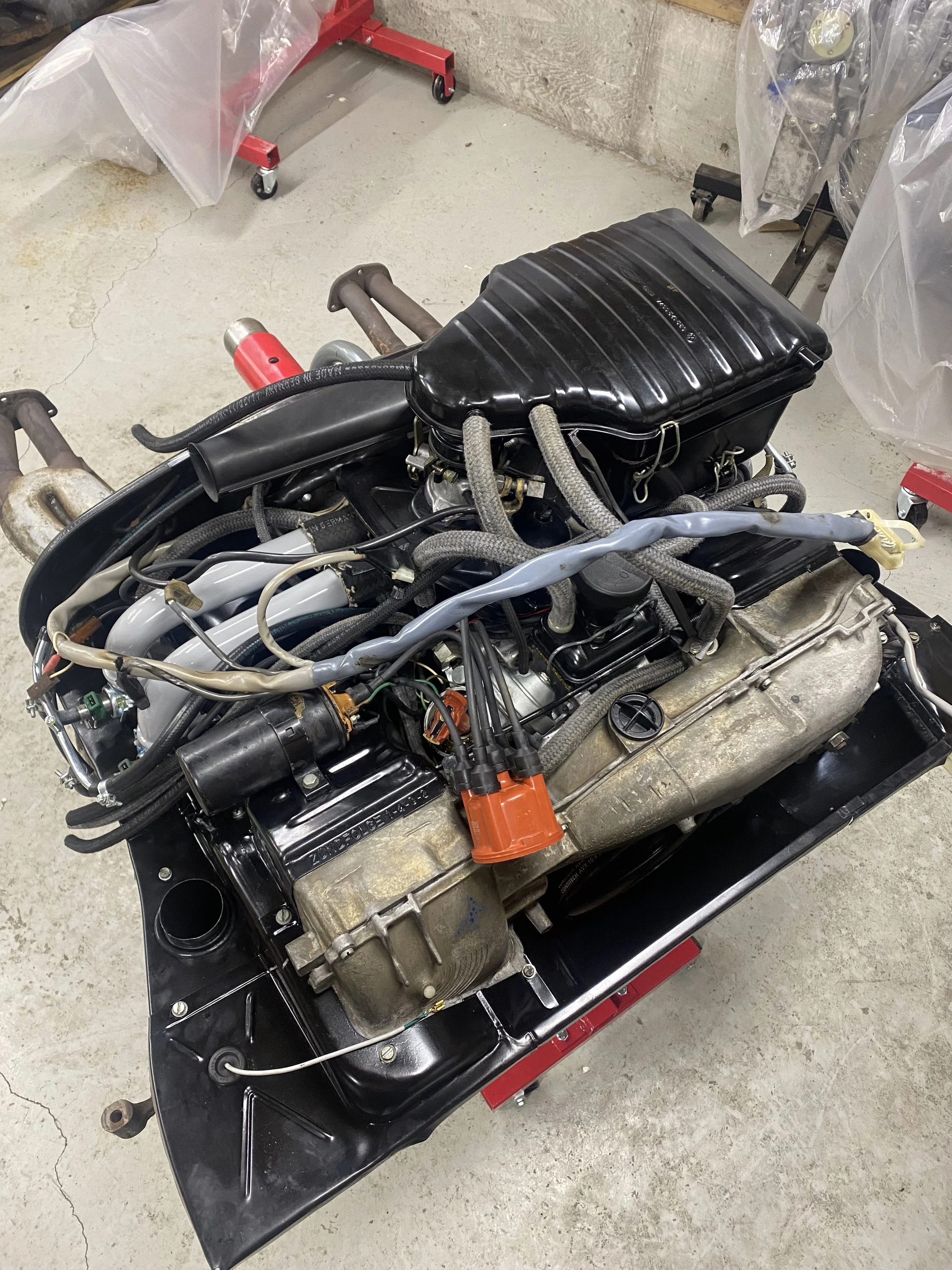 VW type 4 engine on a stand in a garage or workshop with tools and equipment around.