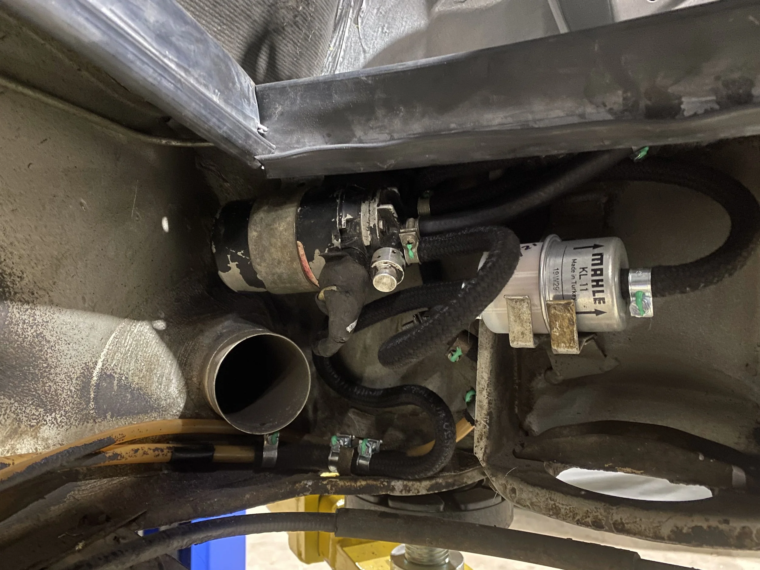 Close-up view of mechanical components including a fuel filter labeled 'MARINE KILHUNE', hoses, and a metal pipe in a confined space.