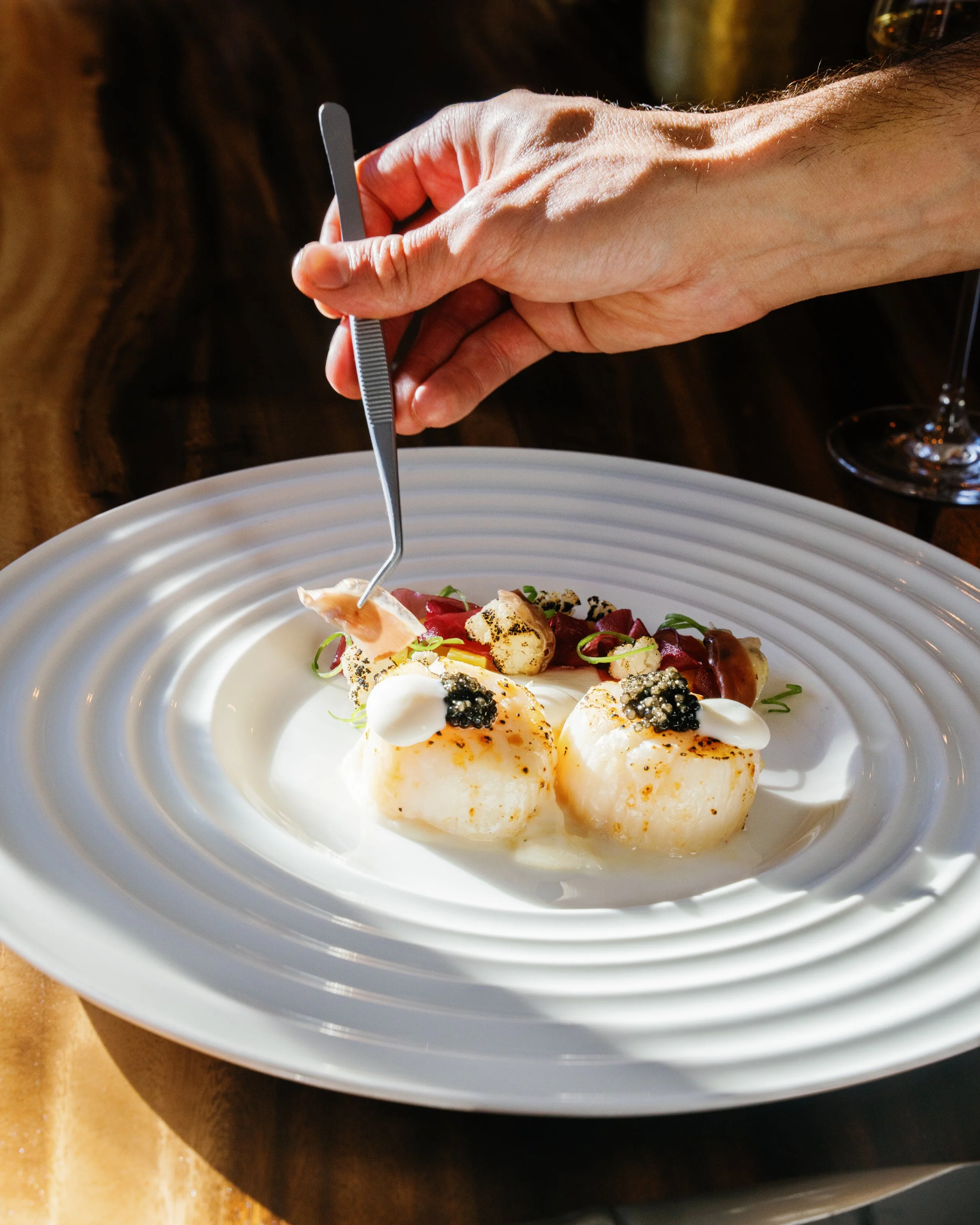 Seared scallops on a white textured plate with Chef Stefano Schiaffino applying final touches of fresh melon shavings at PARC Aspen this winter.
