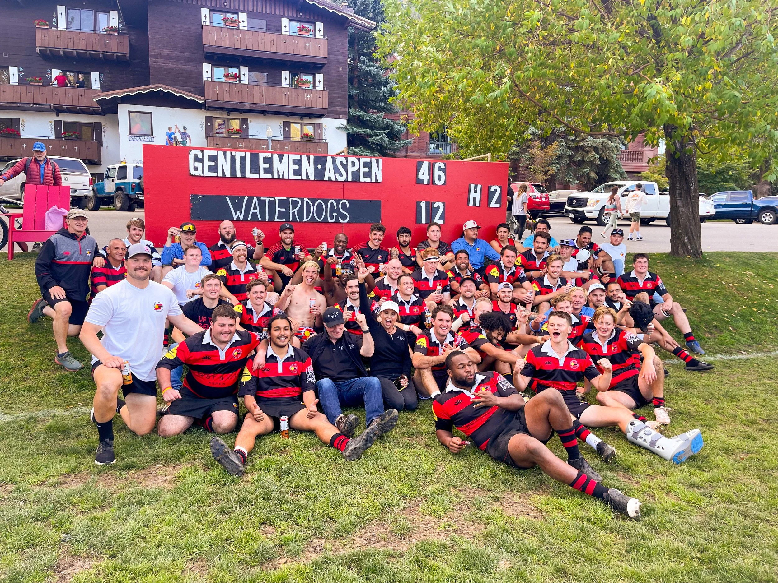 Aspen Gents rugby team laying on the grass in front of the scoreboard after their victory.