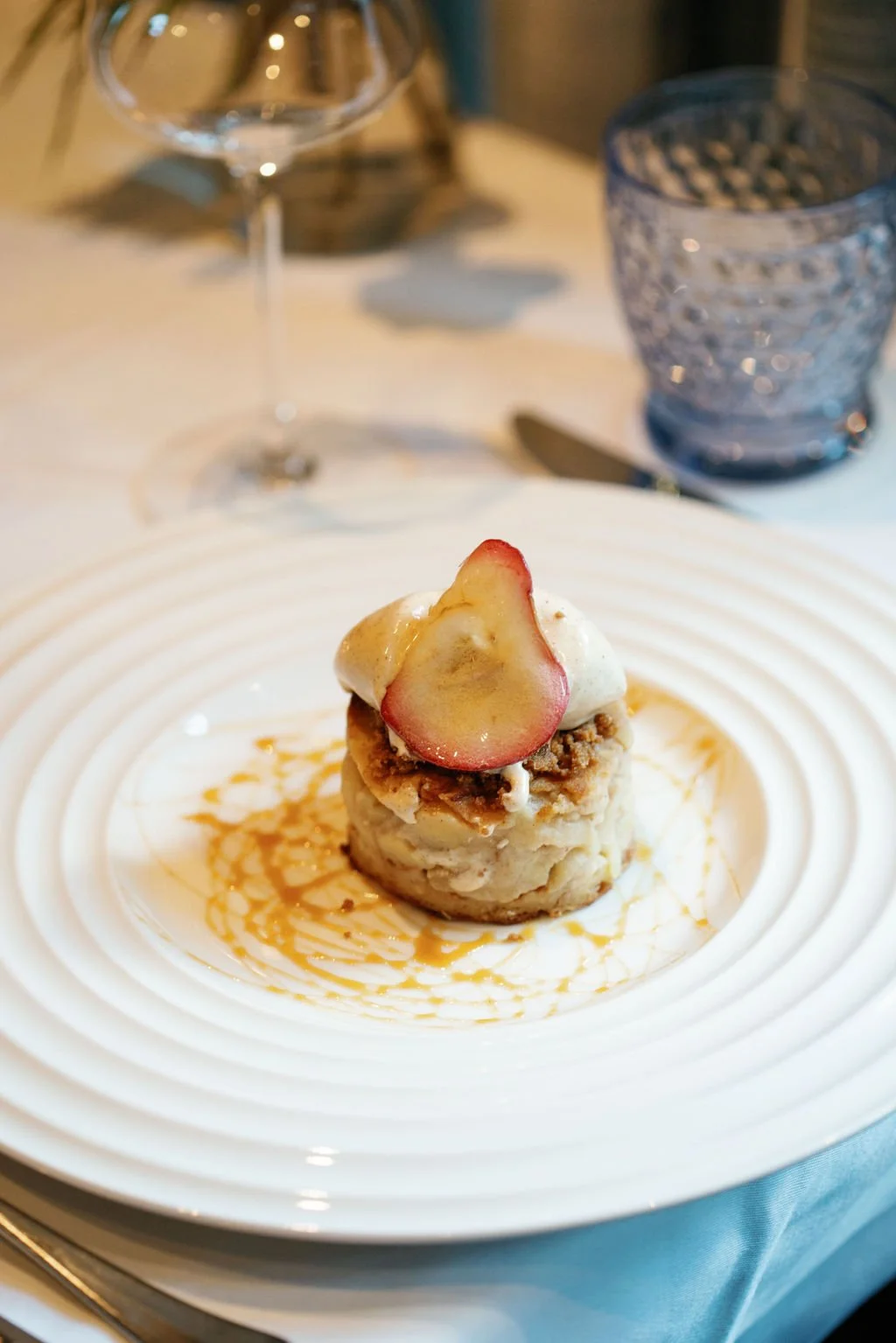 Large white ribbed plate featuring a bread pudding topped with caramelized apples.