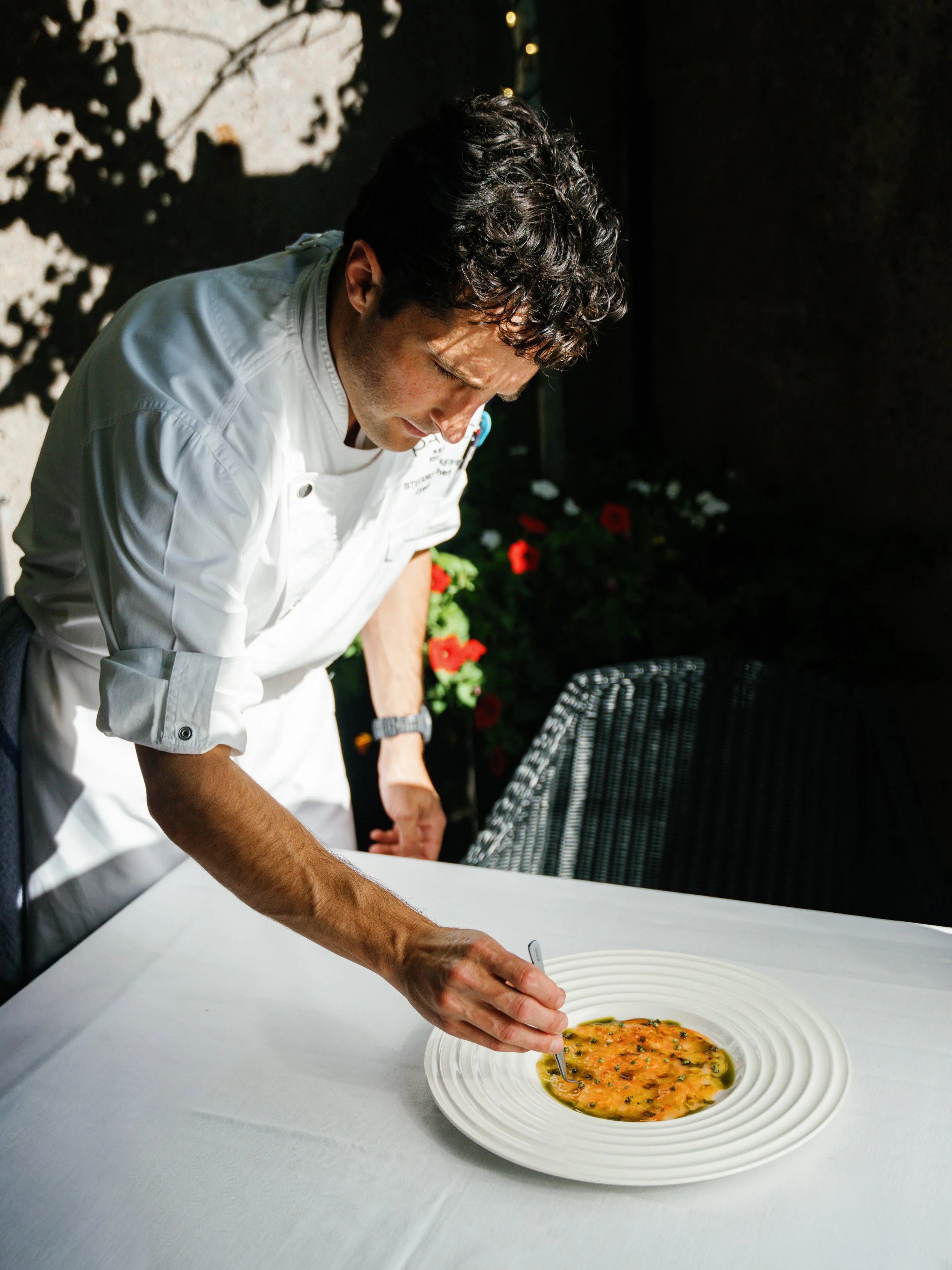 Chef Stefano at PARC Aspen placing the final touches on a Tasting Menu dish on the patio for Autumn.