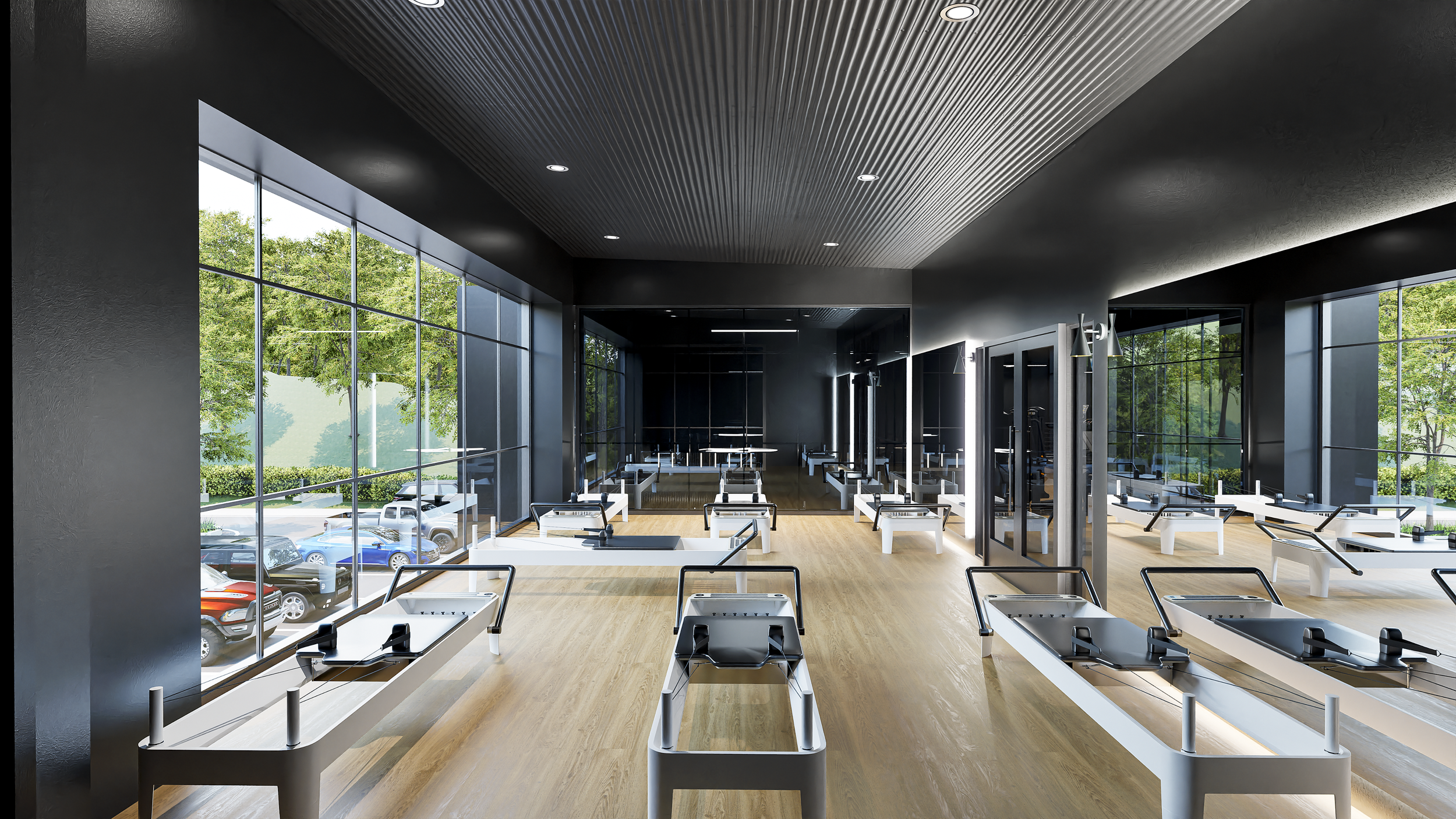 Empty Pilates studio with large windows, black walls, wooden floors, and Pilates reformer machines arranged in rows.