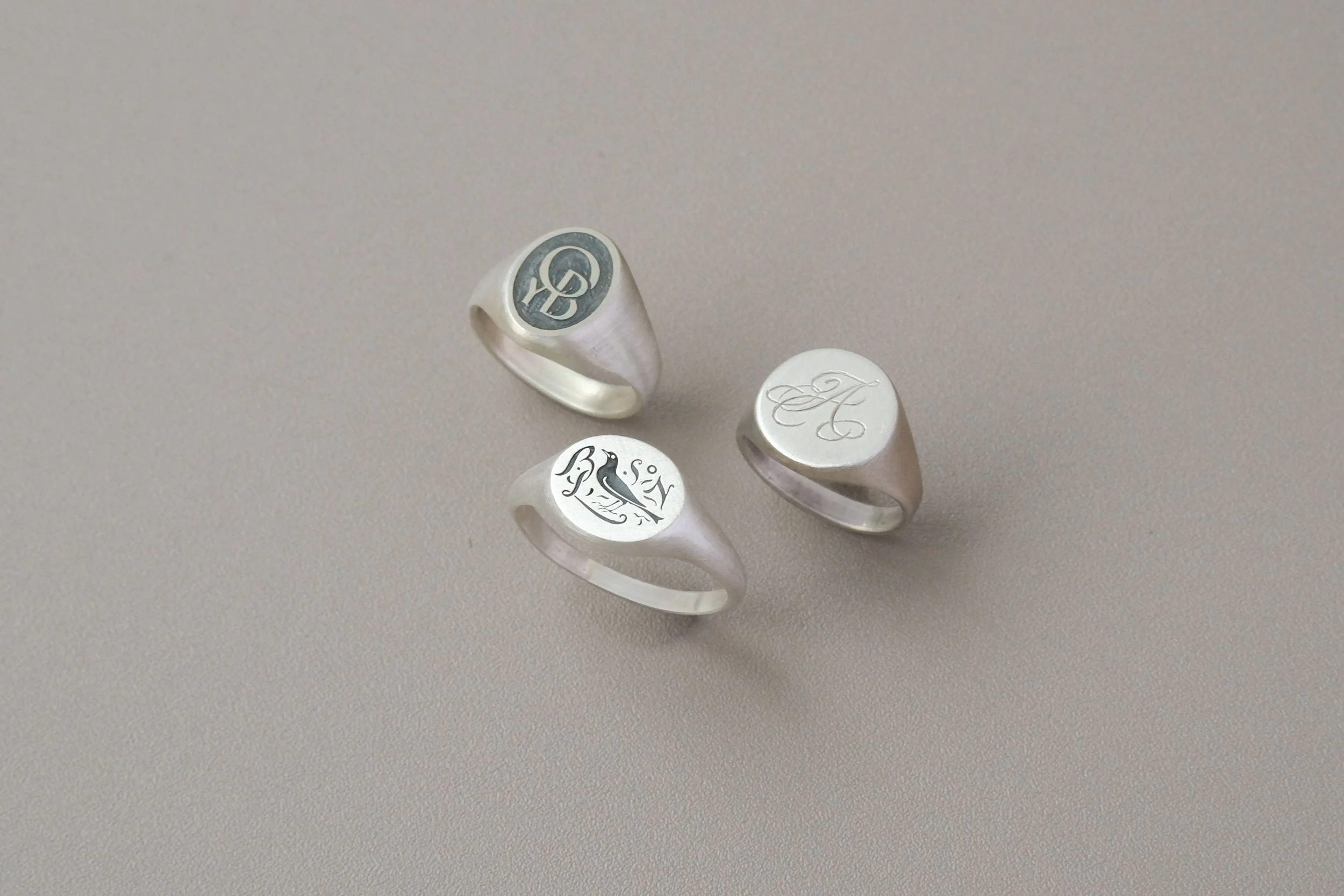 Three silver rings with engraved designs on a plain surface.