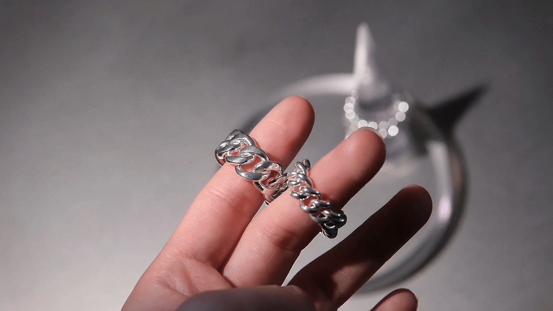 Hand holding a silver chain bracelet in front of a blurred star-shaped object.