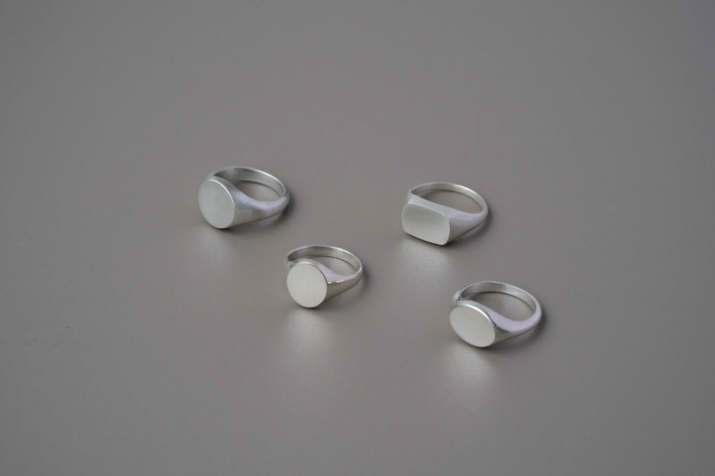 Four silver rings with simple round or flat tops placed on a gray surface.