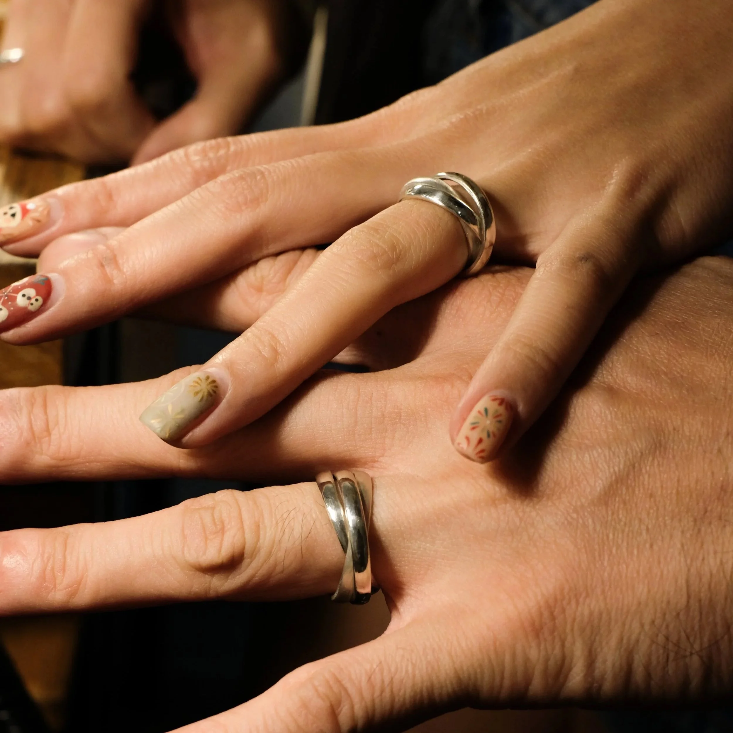 Close-up of three hands showcasing two silver rings on fingers, one hand with Christmas-themed nail art.