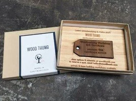 Wooden tags inside a cardboard box on a stone surface.