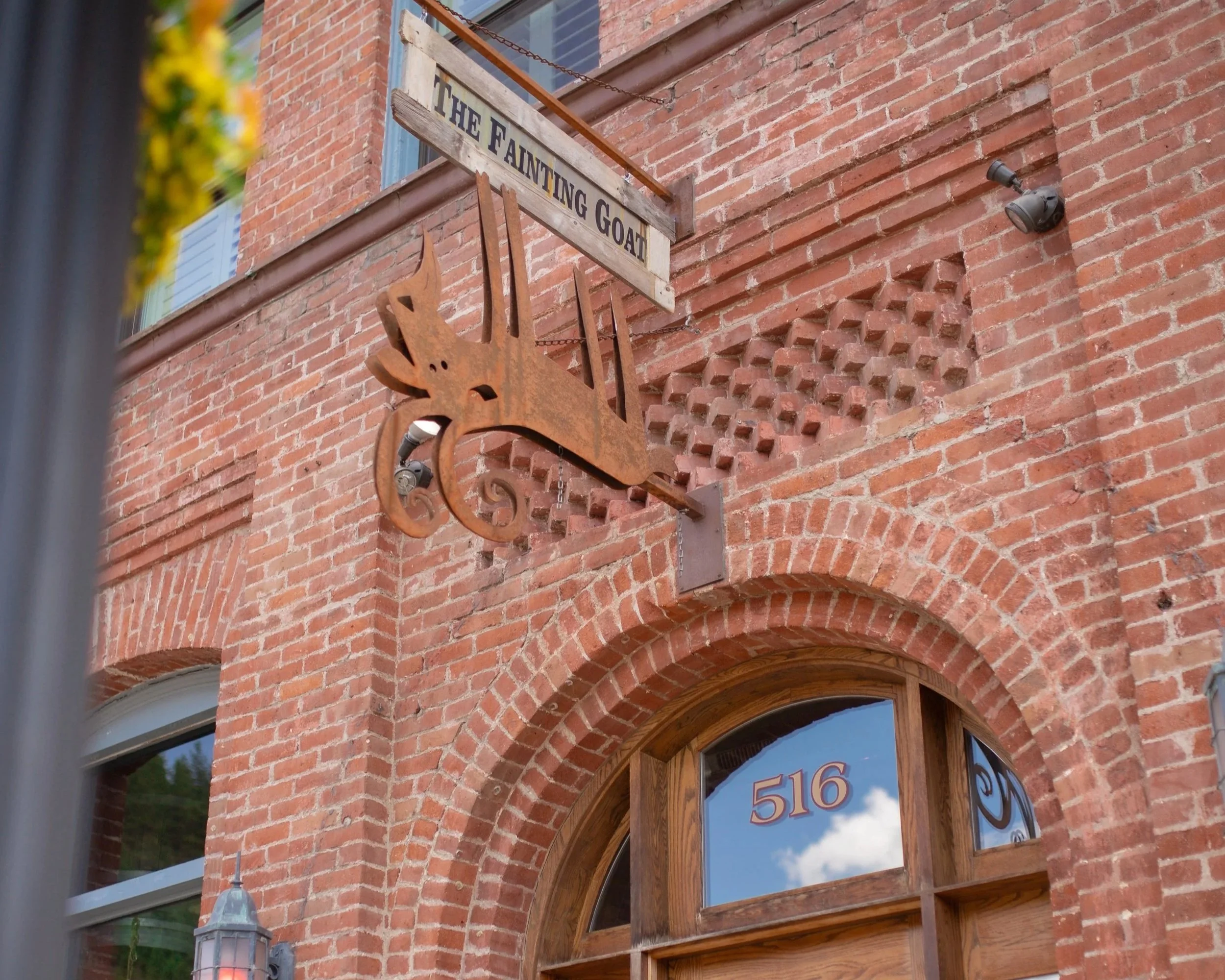 A historic brick building with a hanging metal sign that reads fainting goat