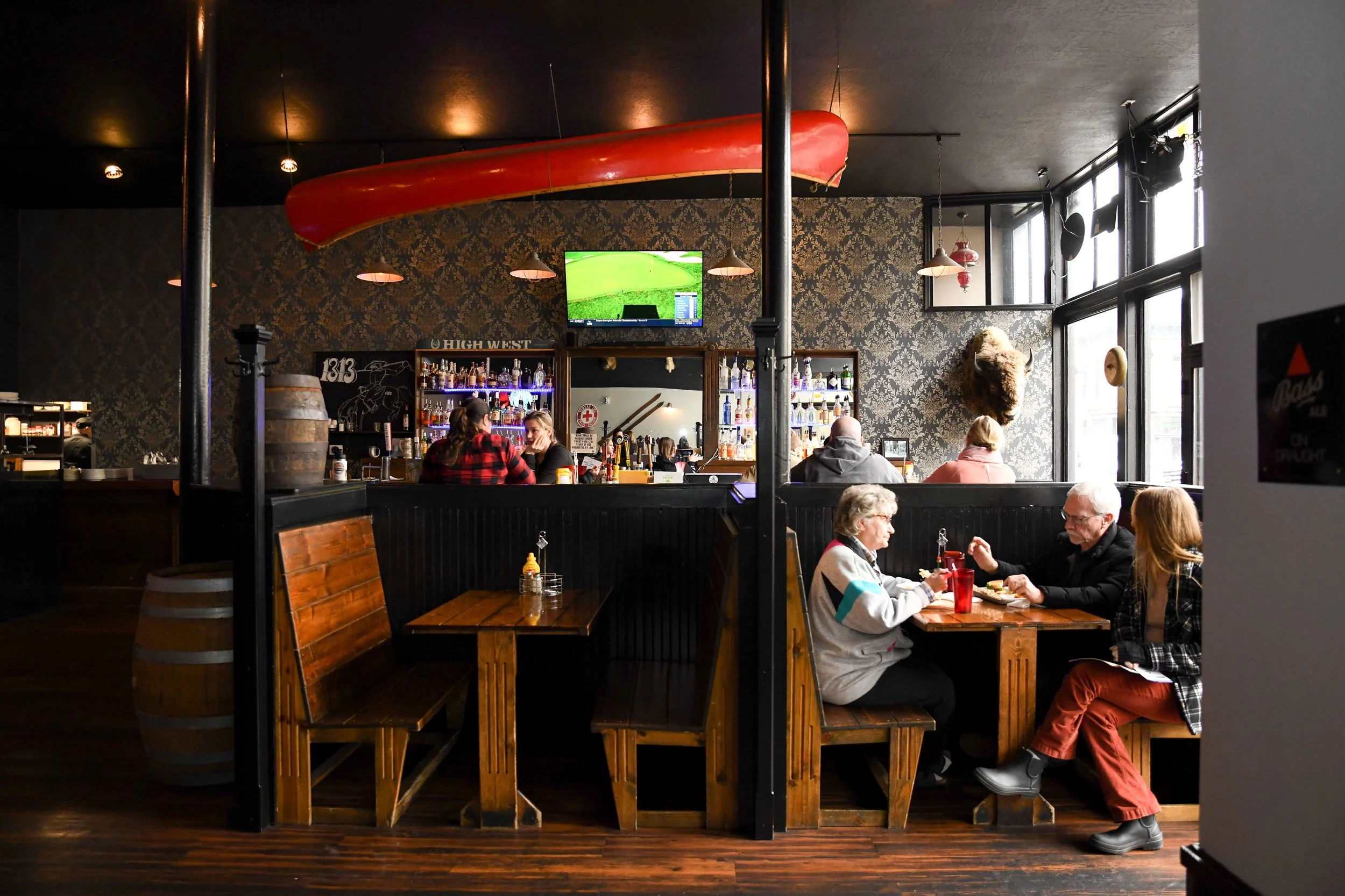 A cozy restaurant with folks sitting at the bar and in a booth table