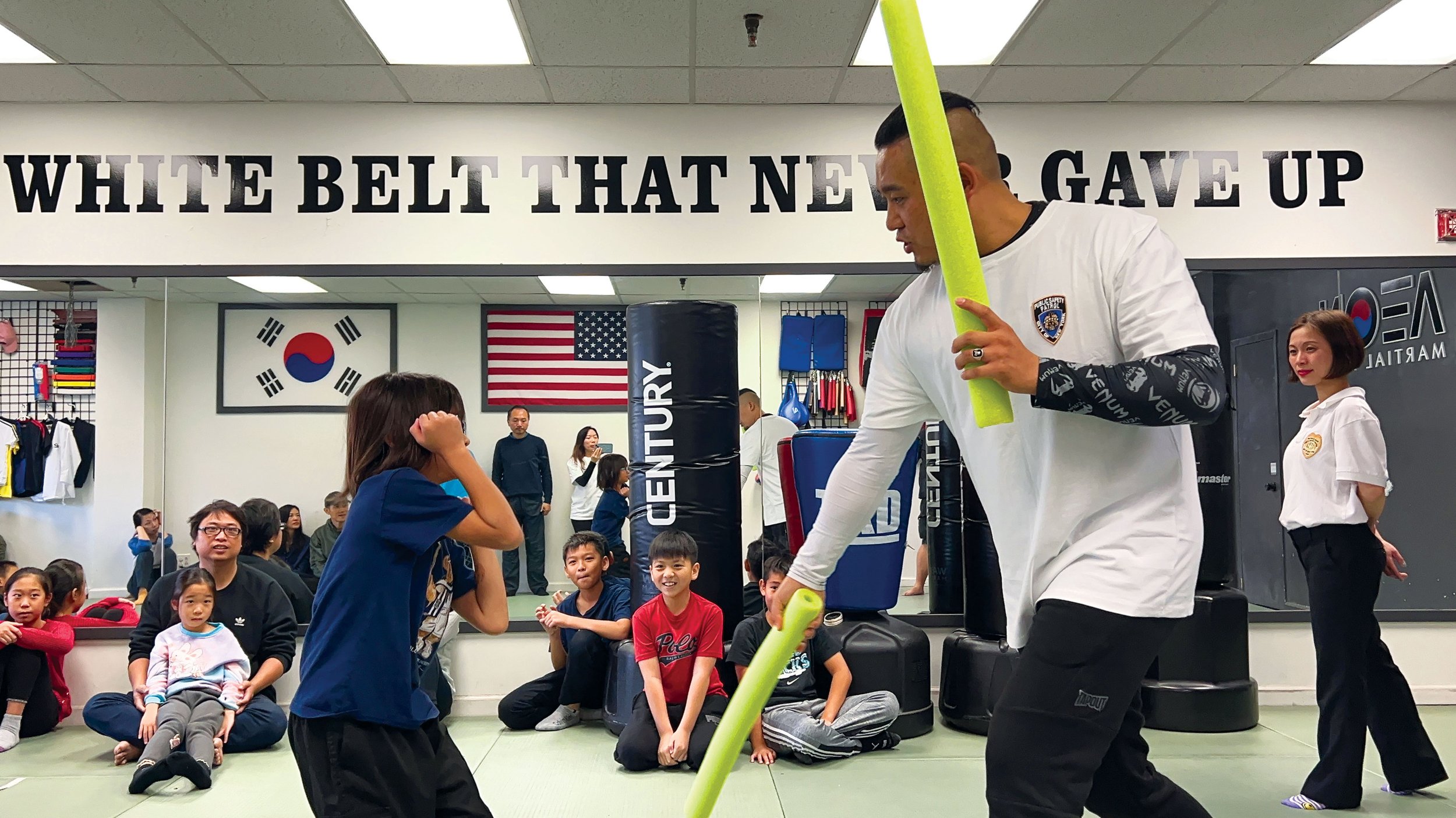 A martial arts instructor provides expert guidiance to a young student during a dynamic training session with foam noodles.