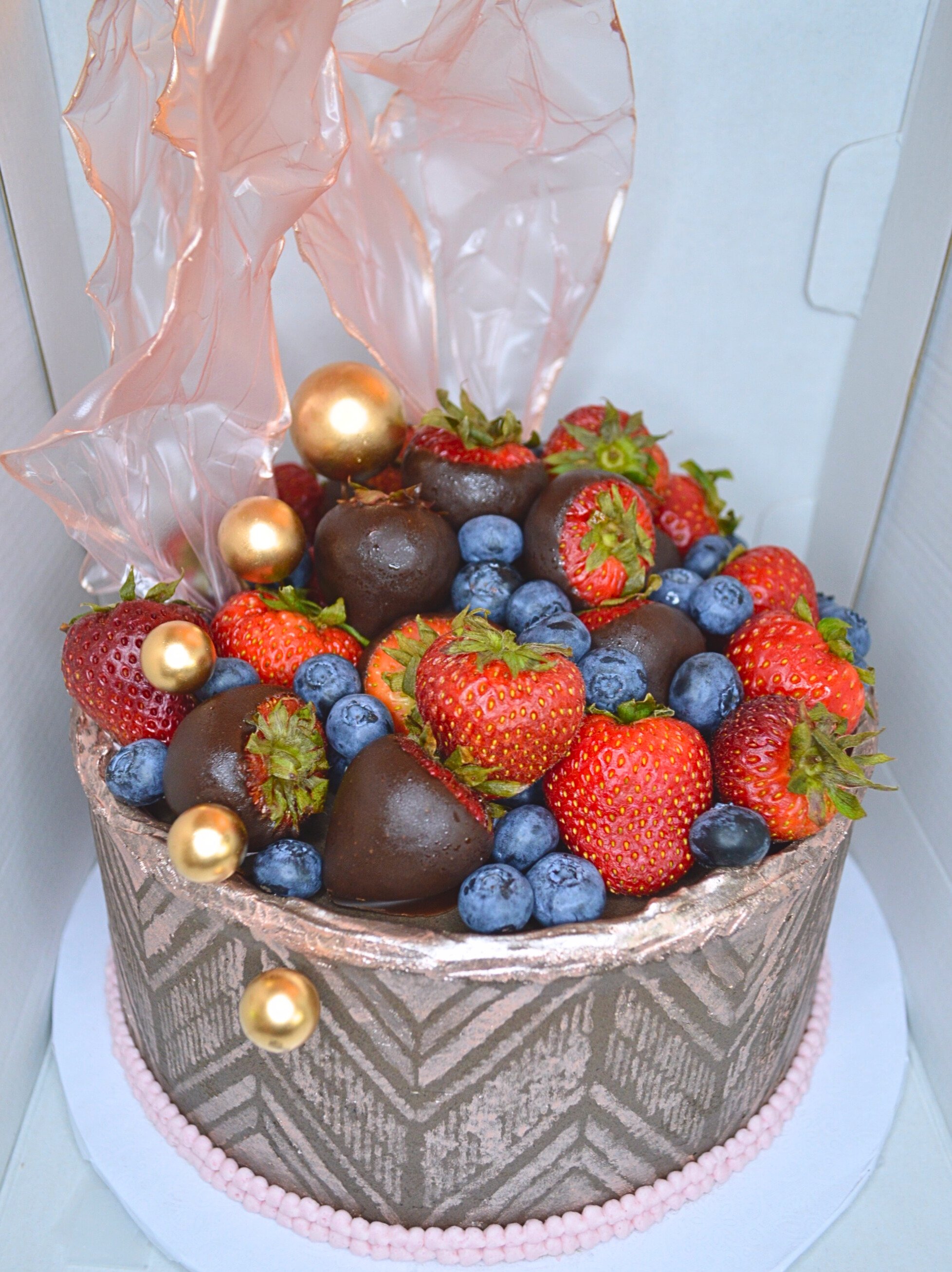 #38. Cake with sails, chevron geometric design in rose gold, fresh blueberries, fresh strawberries, fresh chocolate-dipped strawberries and cake decor balls.