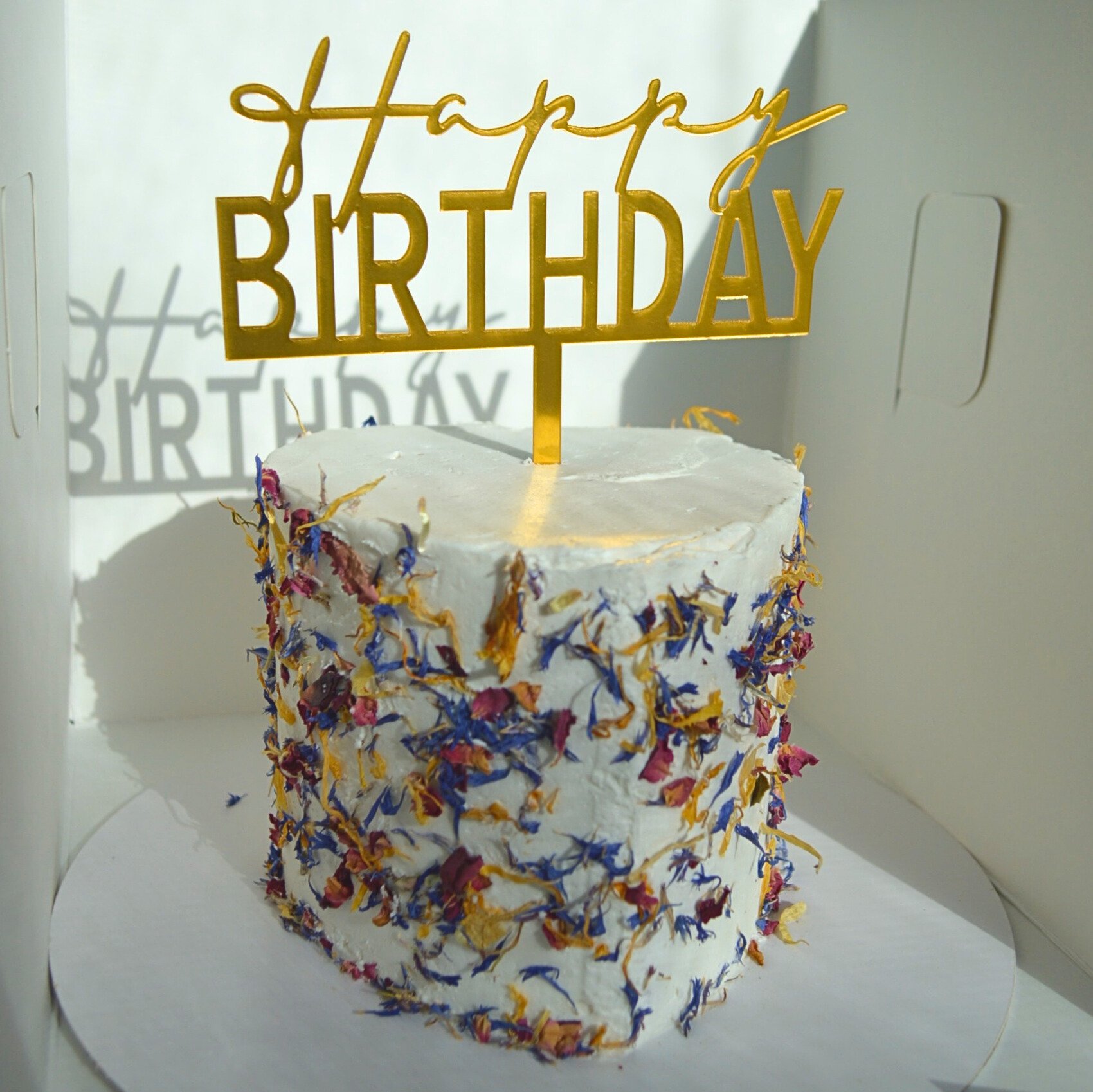 #8. Small heart-shaped cake with edible flower petals and a gold "Happy Birthday" topper.