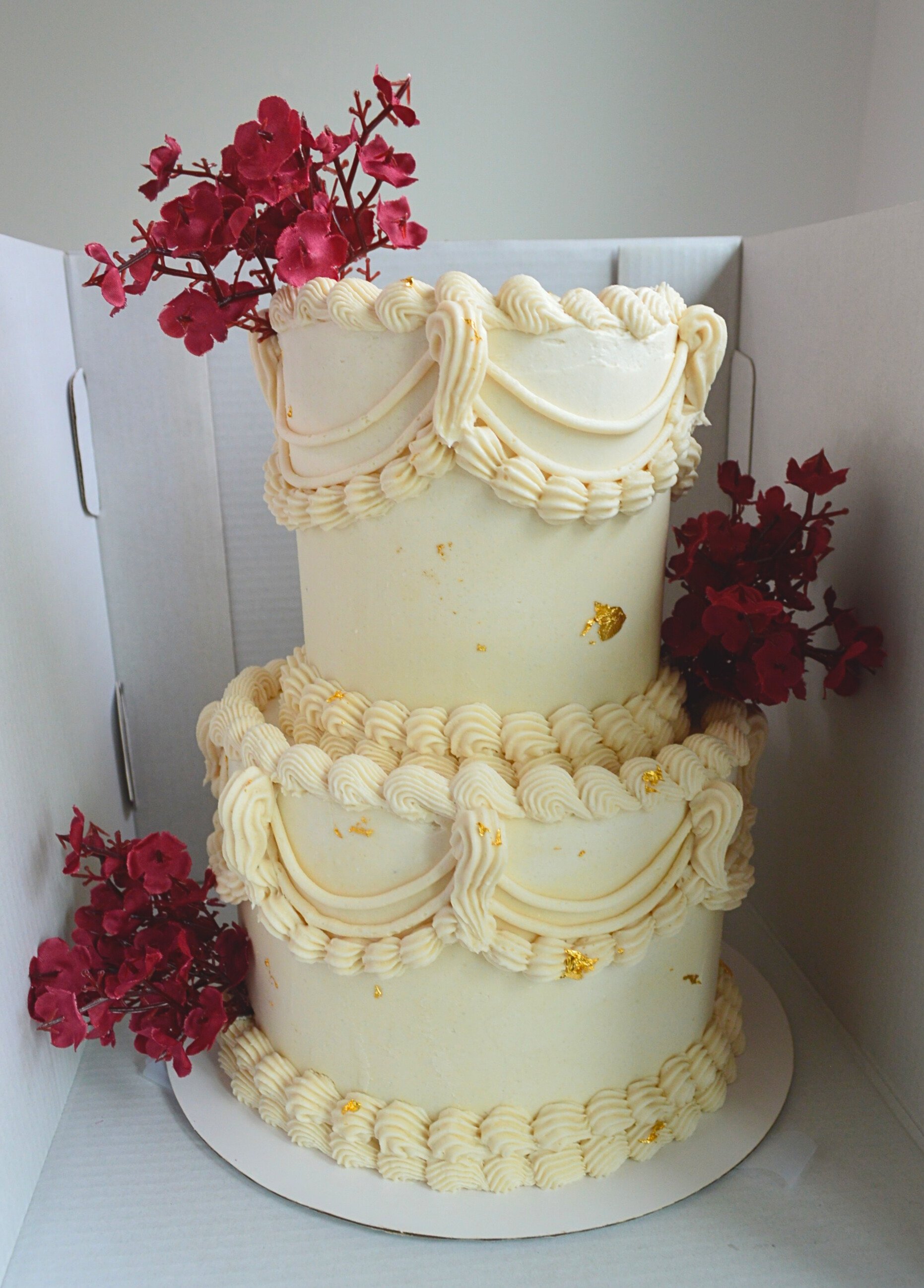#74. Two-tiered beige vintage style cake with edible gold foil and faux florals.