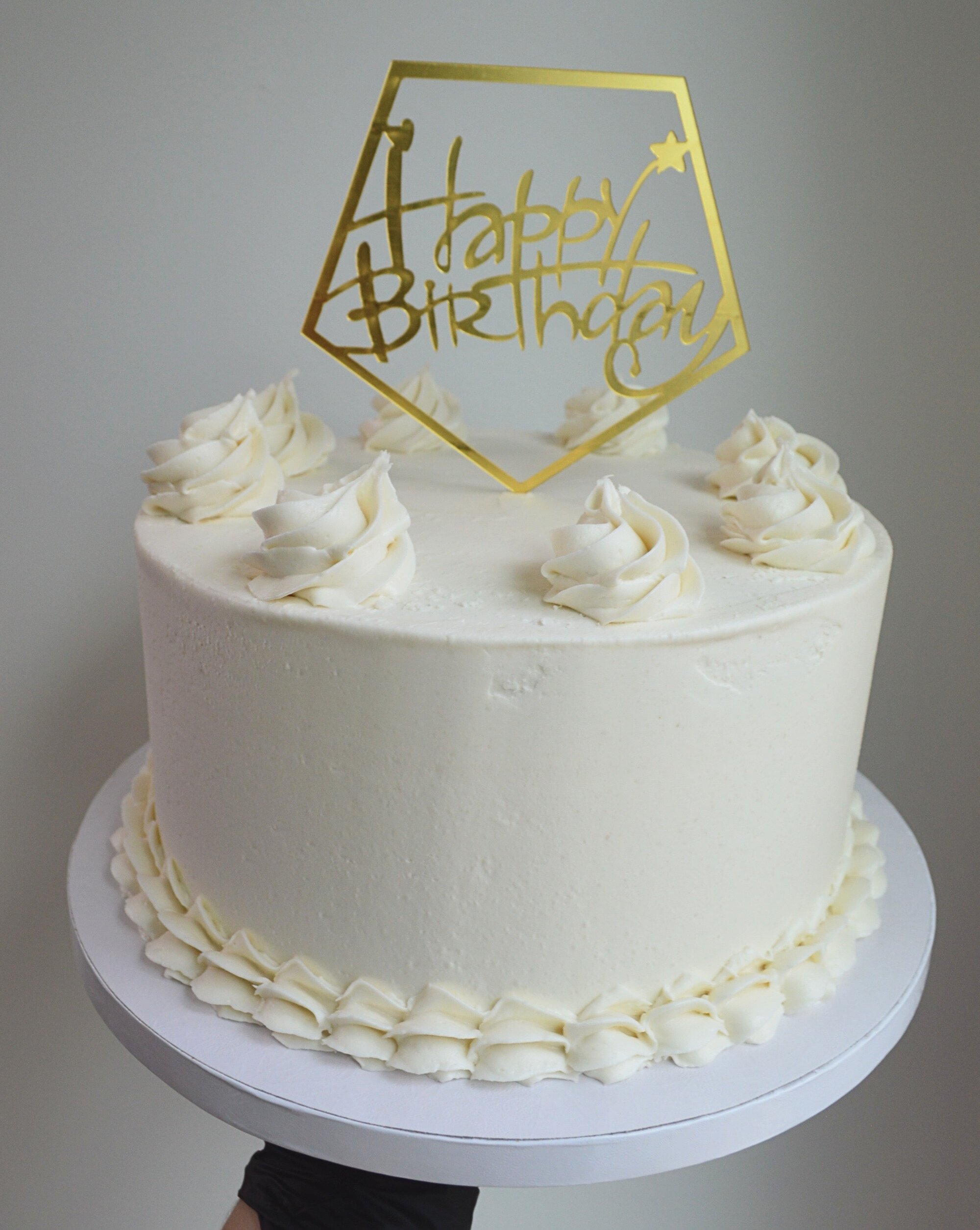#73. Smoothly frosted cake with a bottom border, swirls and a gold "Happy Birthday" topper.