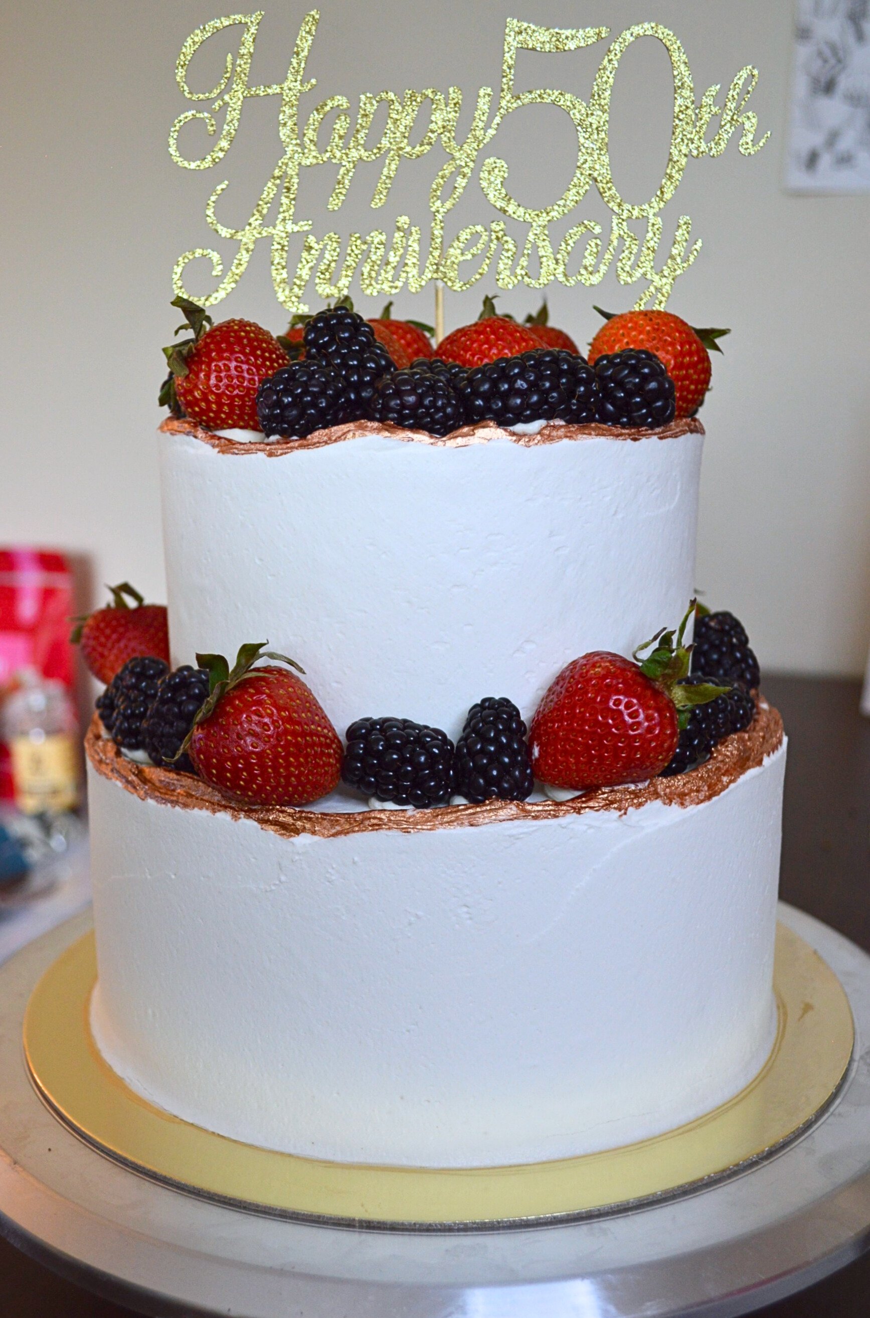 #50. Two-tiered anniversary cake with fresh berries, a natural top ridge and edible bronze paint on the ridge.