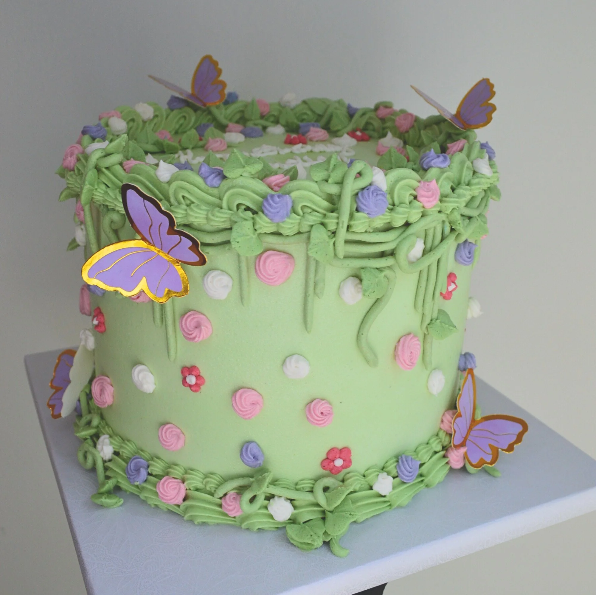 #125. This is an 8" round, 3-layer whimsical butterfly cake with vines, shell borders and small hand-piped frosting flowers.