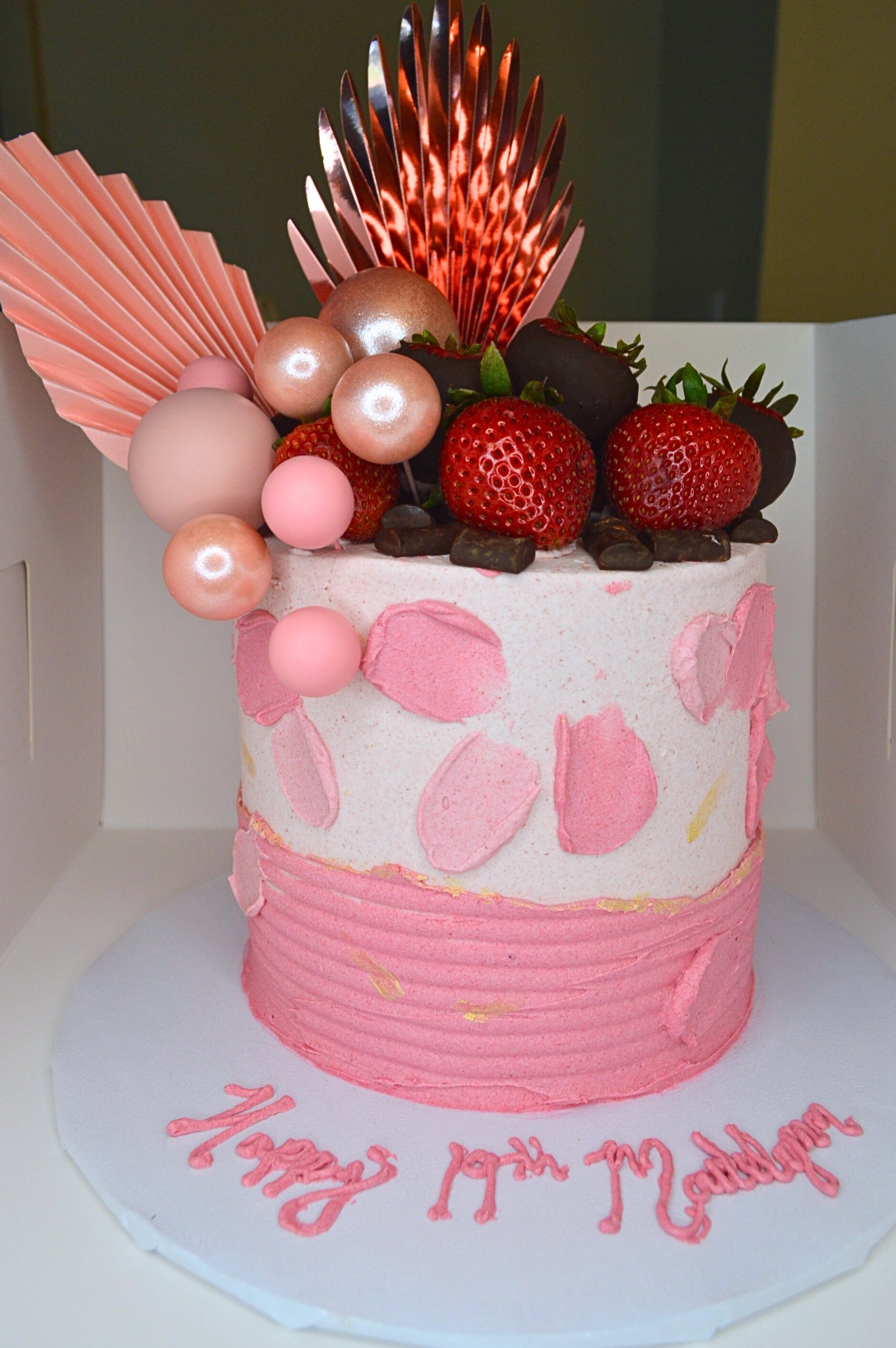 #36. Pink cake with a darker pink ridged overlay, pink frosting swipes in, edible gold paint, fresh strawberries, chocolate chunks, custom cake decor and a custom message on the cake board.