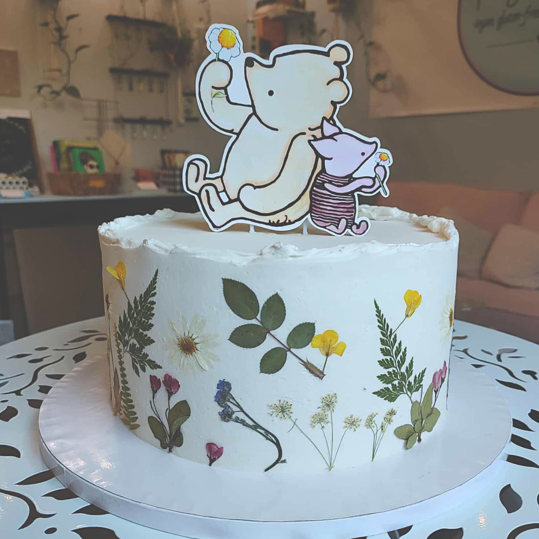 #99. This is a 10" round, 3-layer Winnie the Pooh cake with real, pressed, food safe wild flowers around the outside of the cake.