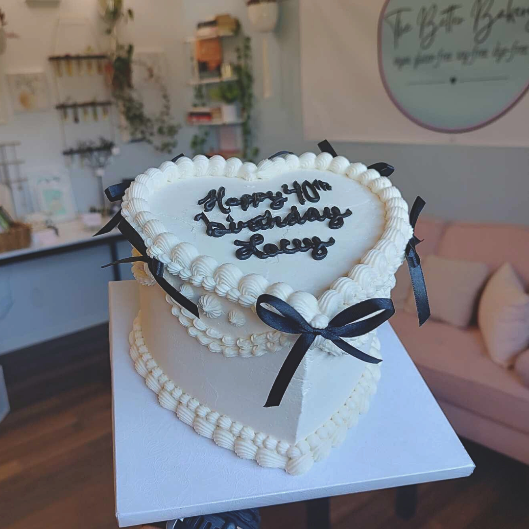 #90. This is a 6" heart-shaped, 3-layer vintage style cake with black ribbon bows.