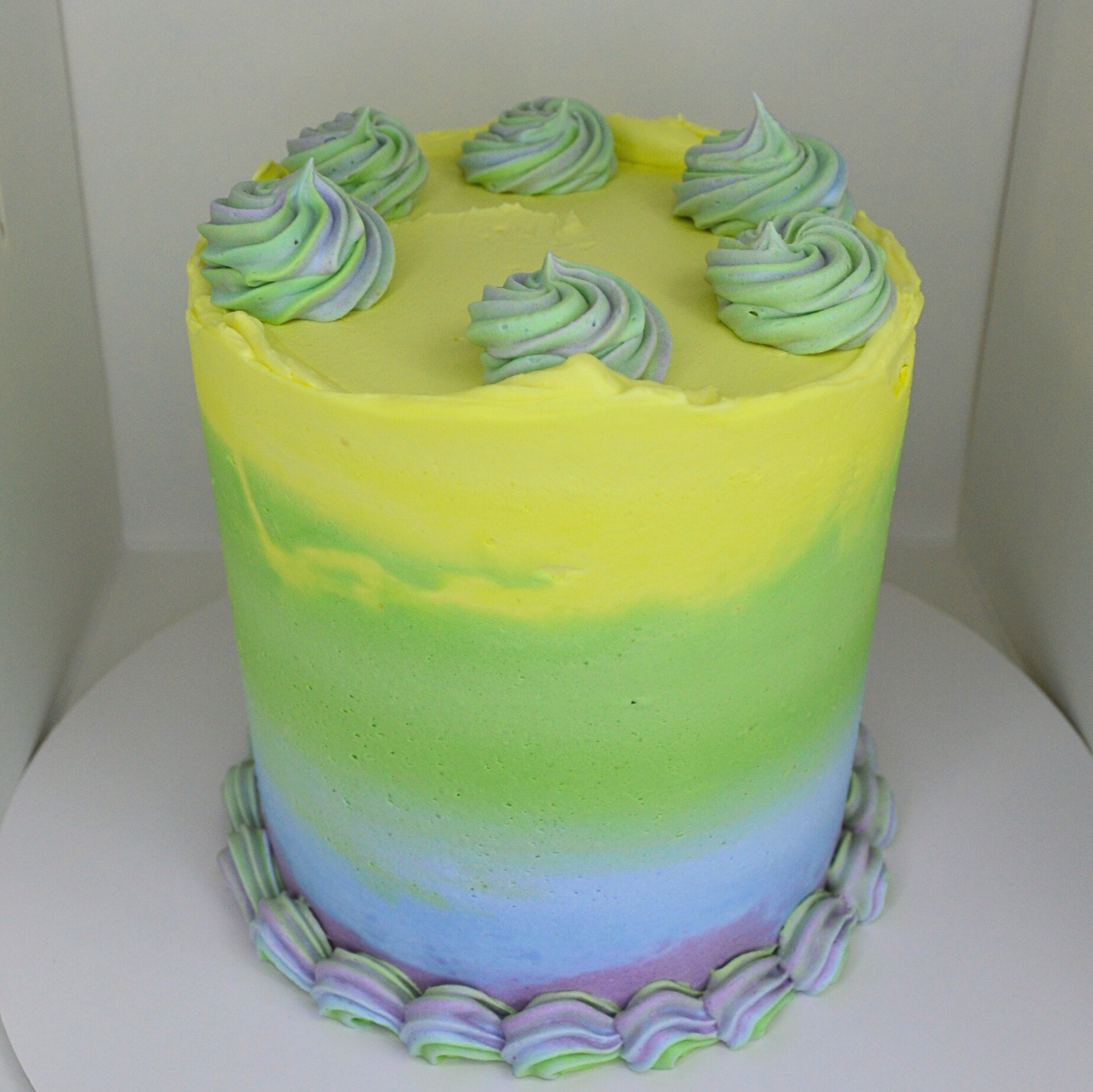 #69. 4" round, 3-layer rainbow ombre cake with a rainbow bottom border, a natural top ridge and swirled green and purple swirls.