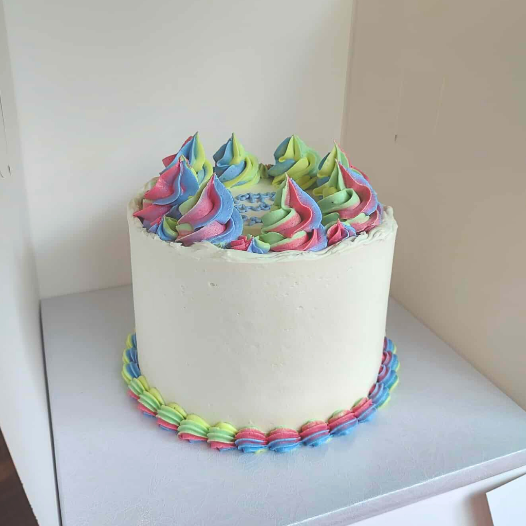 #97. This is a 6" round, 3-layer white cake with a rainbow bottom shell border and rainbow frosting swirls.