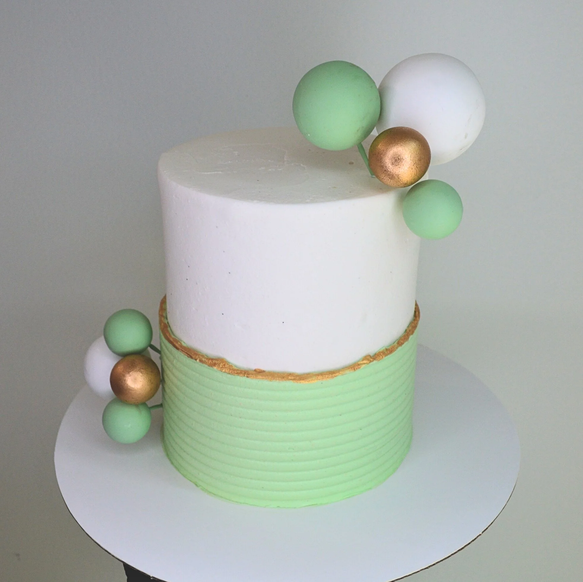 #127. This is a 4" round, 3-layer white cake with a green ribbed overlay, edible gold paint over the top edge of the overlay, and cake ball decor.