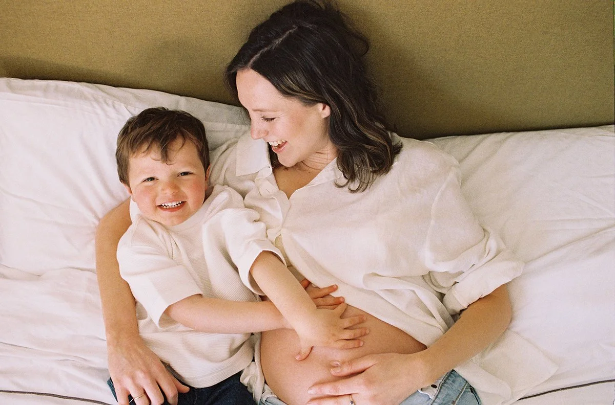 Analogue documentary portrait of a pregnant mother and her young son cuddling in bed.