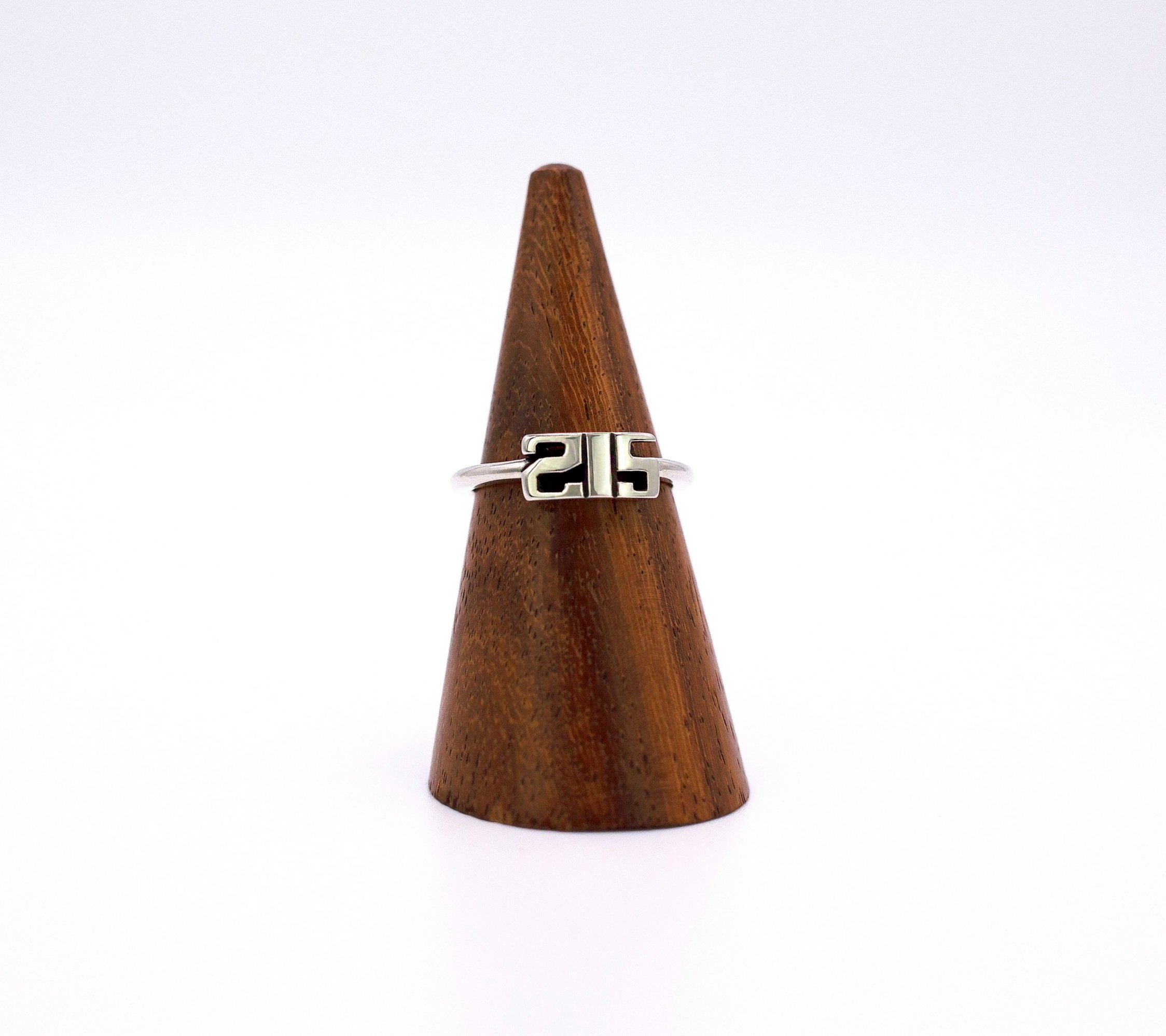 Front view of sterling silver ring with thin band and a small motif depicting the number 215 in bold font.