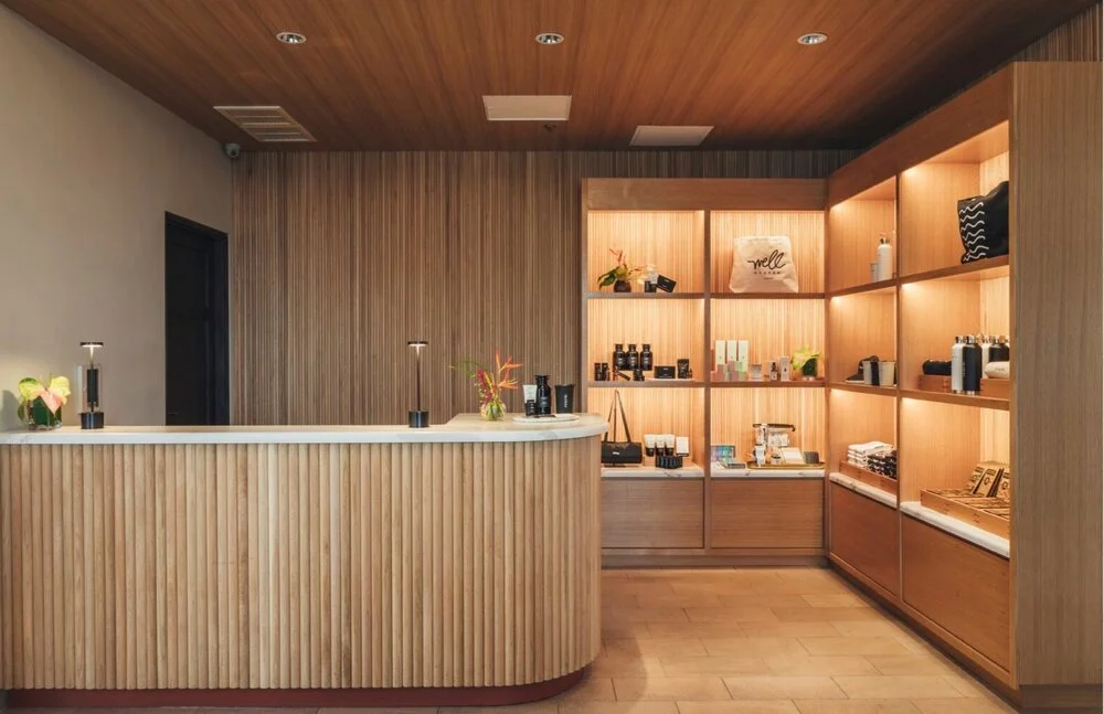 Reception area with wooden counters and shelves displaying various products, including bags, bottles, and decorative plants.