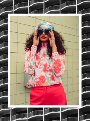 Fashionable woman in floral outfit with sunglasses, colorful headscarf, and pink pants against a tiled wall, surrounded by a border of building balconies.
