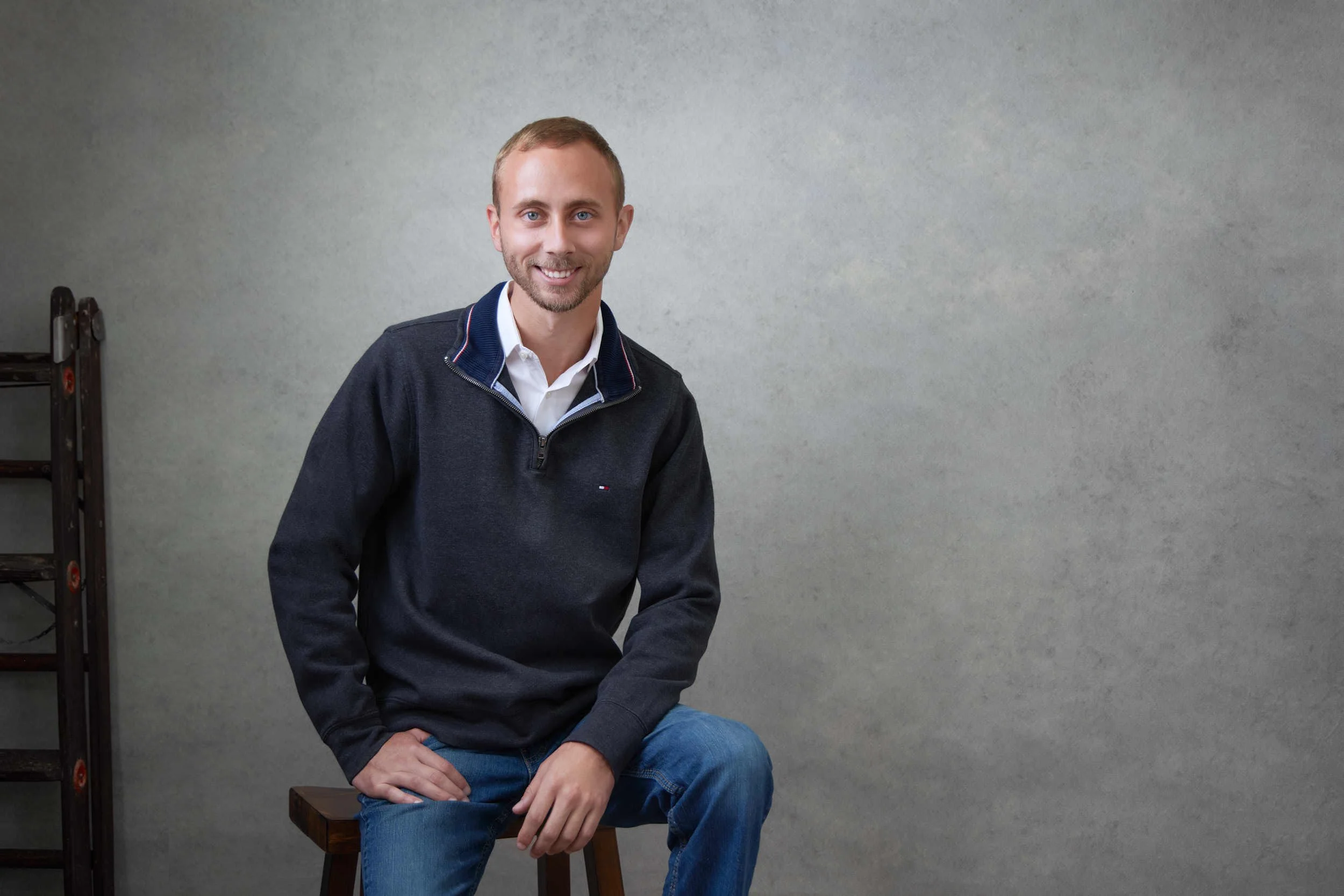 Relaxed professional portrait of a man seated against a textured gray background.