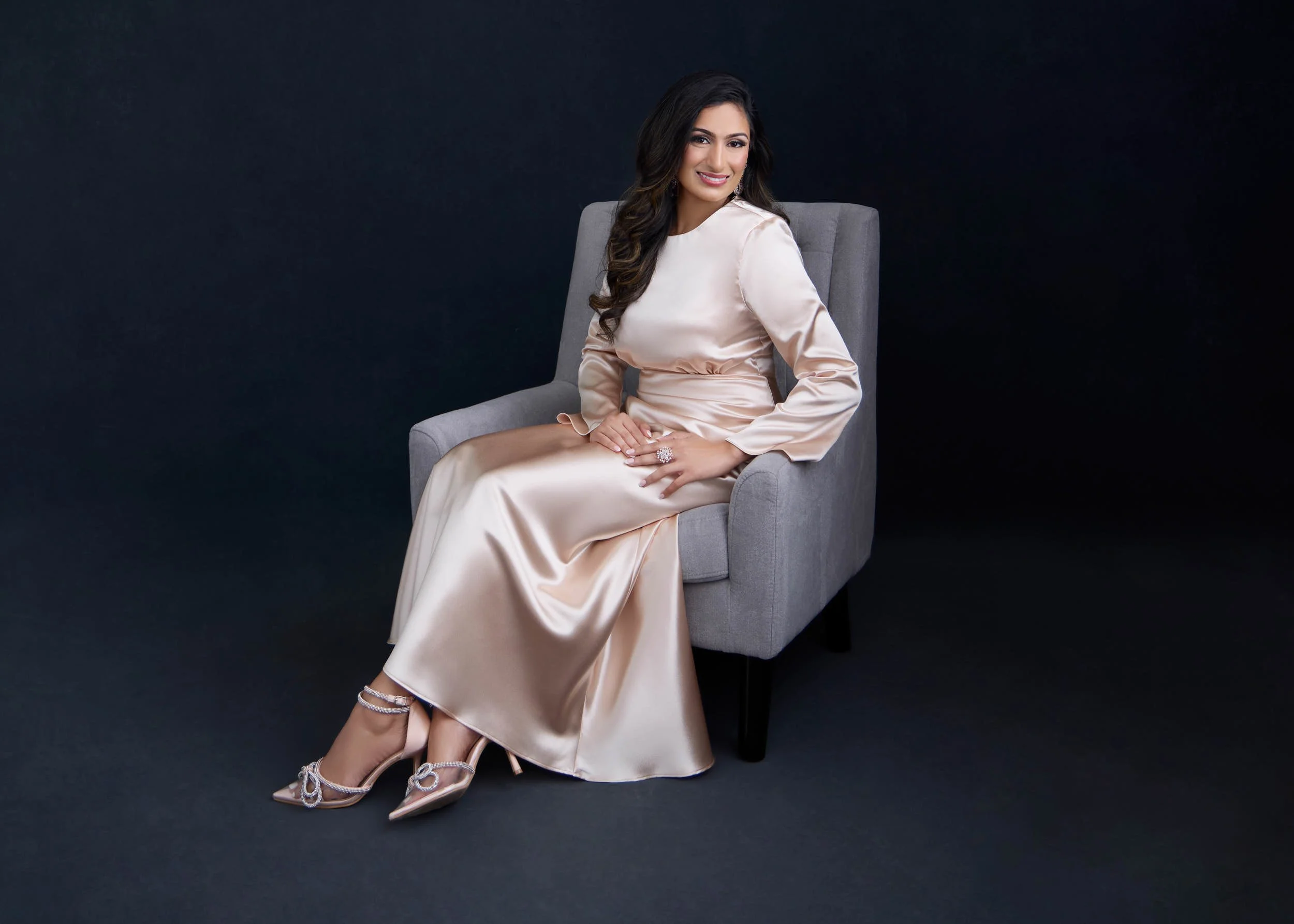 Full-length personal brand portrait of a woman seated in a chair wearing a formal neutral dress.