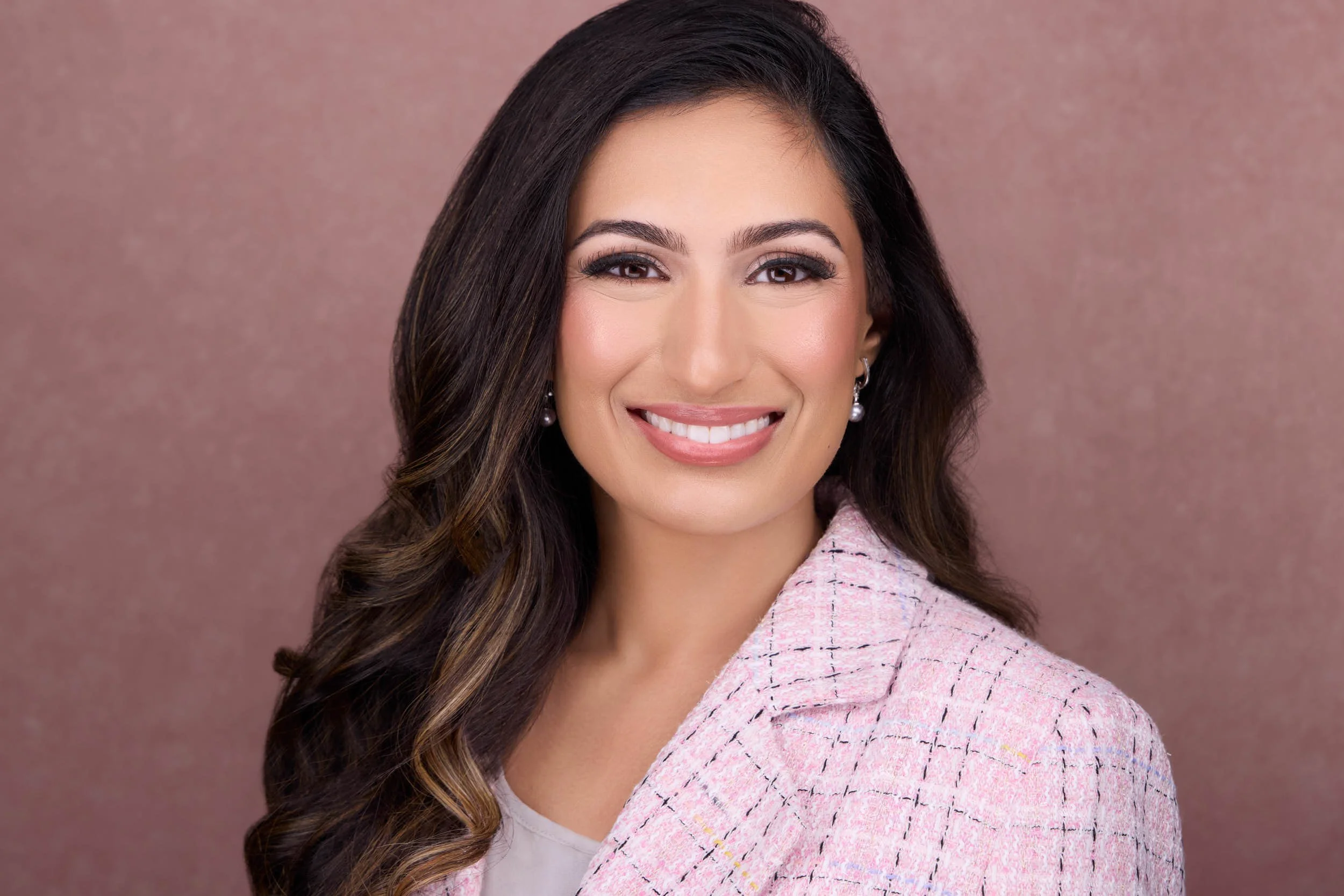 Professional portrait of a woman in a pink blazer against a coordinating pink background.