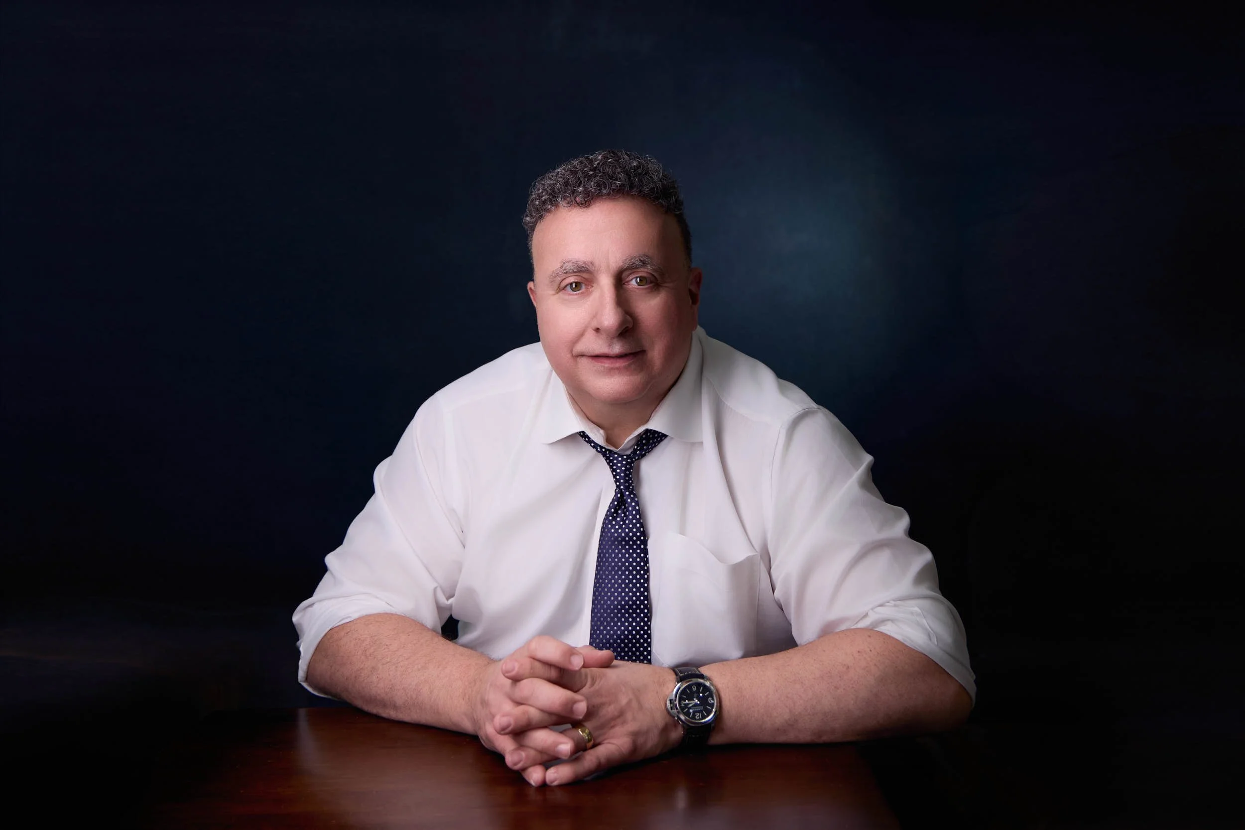 Environmental executive portrait of a man seated at a table in a white shirt and tie.